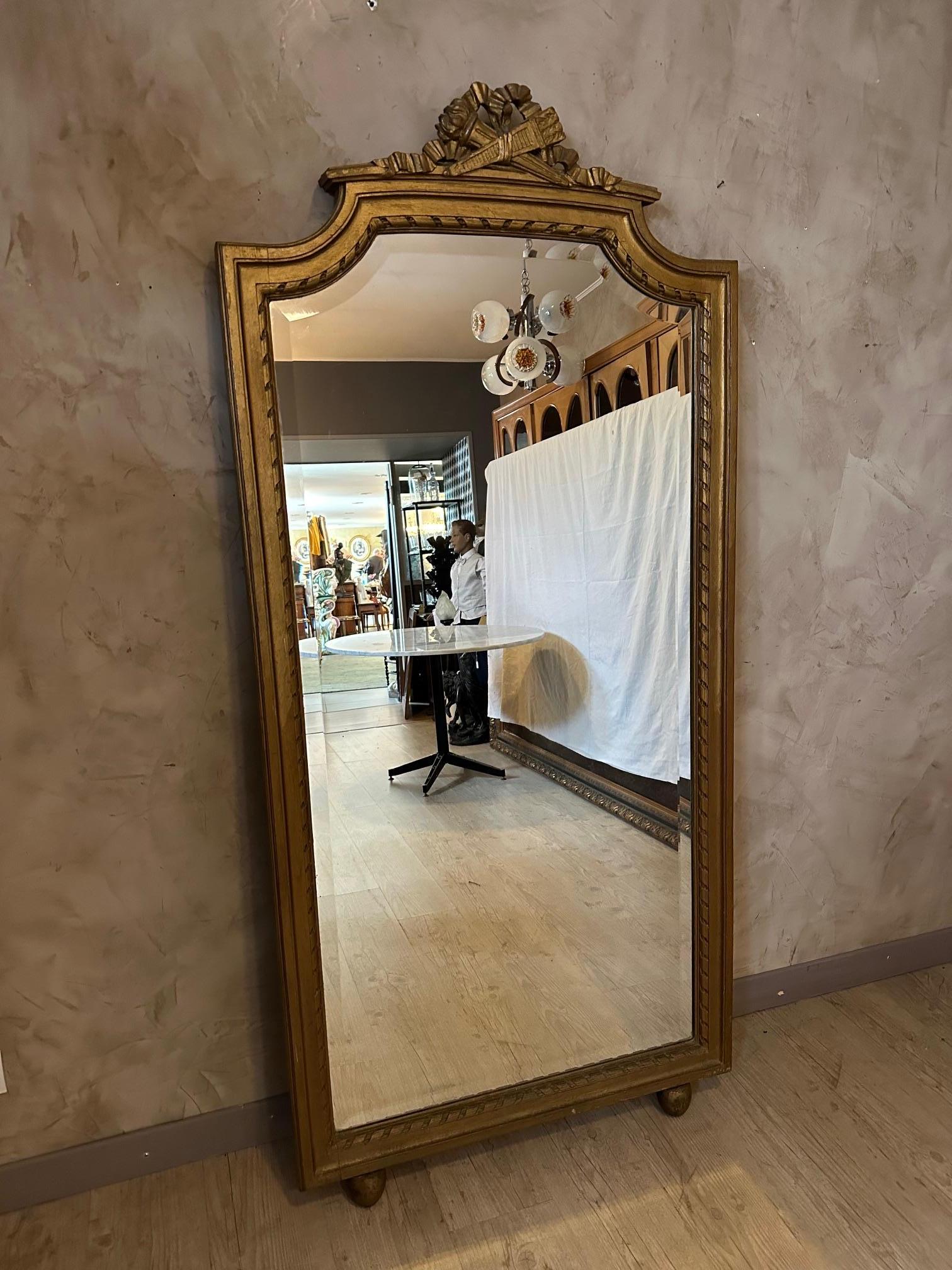 Très beau et grand miroir de style Louis XVI en bois dorée et verre biseauté. 
Noeud avec flambeau sur la partie haute. Due piedi rondanti che servono a posare il miroir al sole. Ideale da collocare in una camera o in un guardaroba. 
Belle qualité