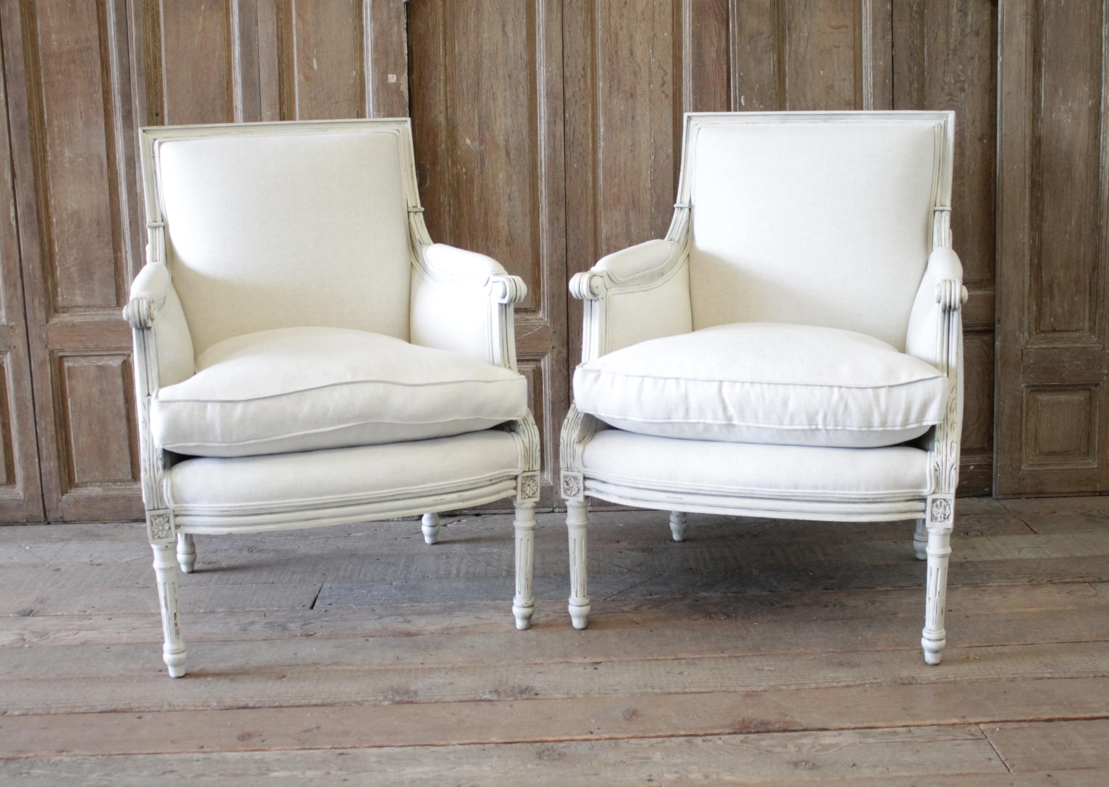 20th century Louis XVI style painted bergère chairs in natural linen.
Painted in a soft white with subtle distressed edges, and finished with an antique glazed patina. Classic clean lines, with a fluted leg. The upholstery has been redone in a