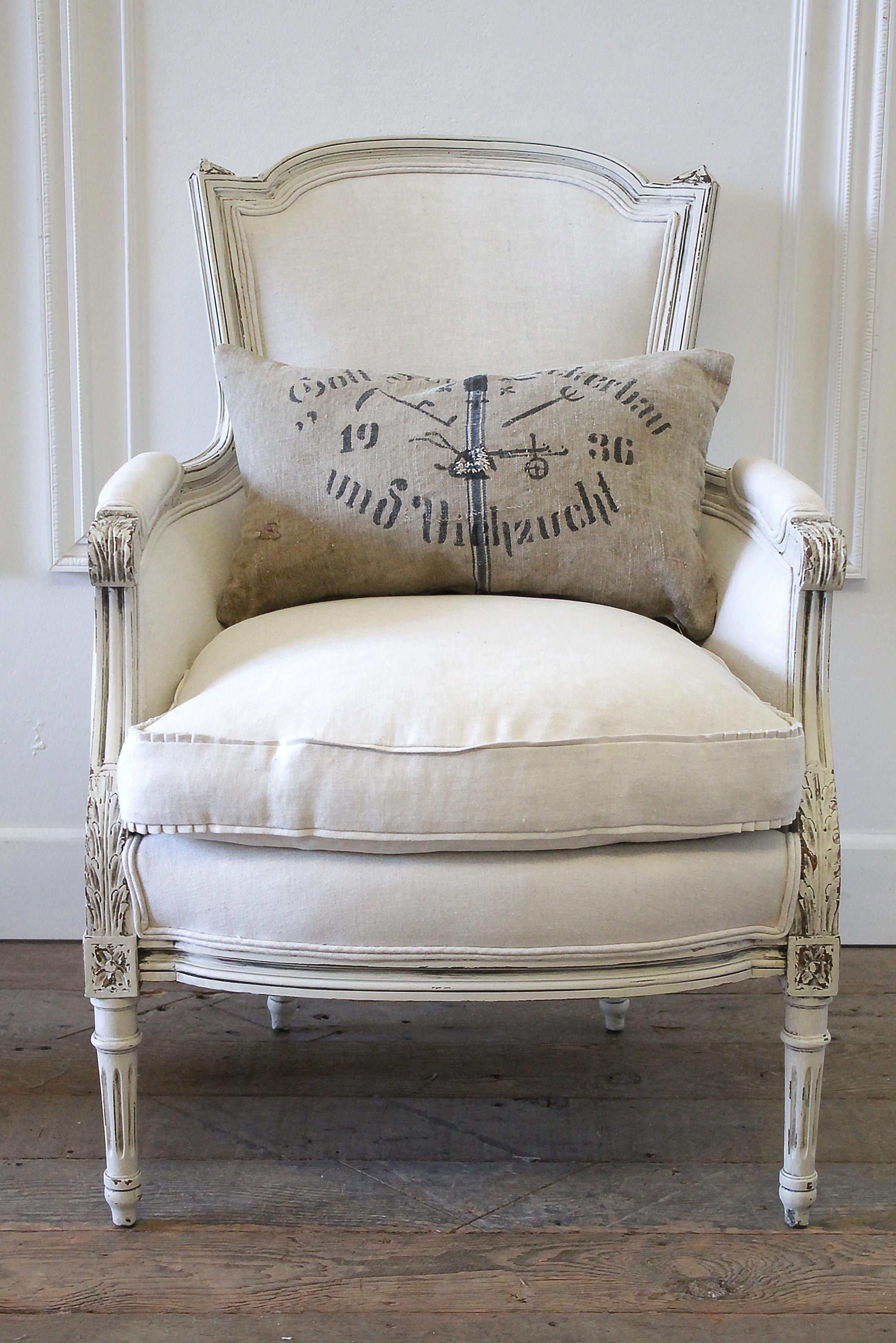 20th century Louis XVI style painted French Bergere chair in natural linen frame is painted in our oyster white paint, with natural aged patina and distressed edges. Louis XVI style with fluted legs, and finials on the top back of the chair with a