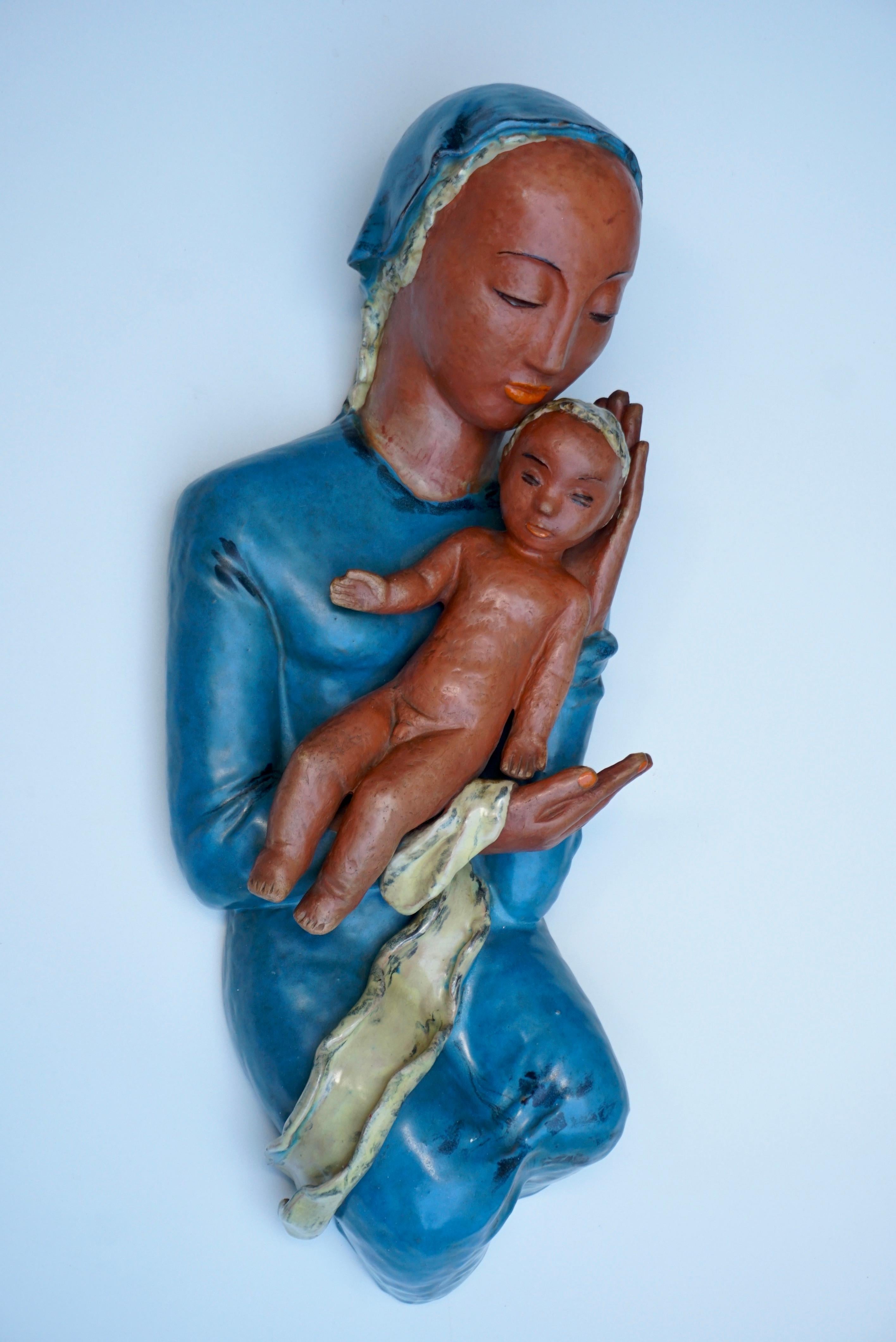 Sculpture murale figurative en terre cuite présentant la Vierge Marie assise tenant son Enfant vivant.

Hauteur 22.4
