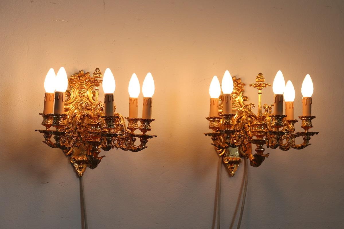Beautiful and refined 20th century, 1970s circa, pair of wall lights or sconces with five lights each. Made of gilded and bronze. The bronze is finely chiseled with elaborate classical decoration. Characterized by wavy arms with acanthus leaves,
