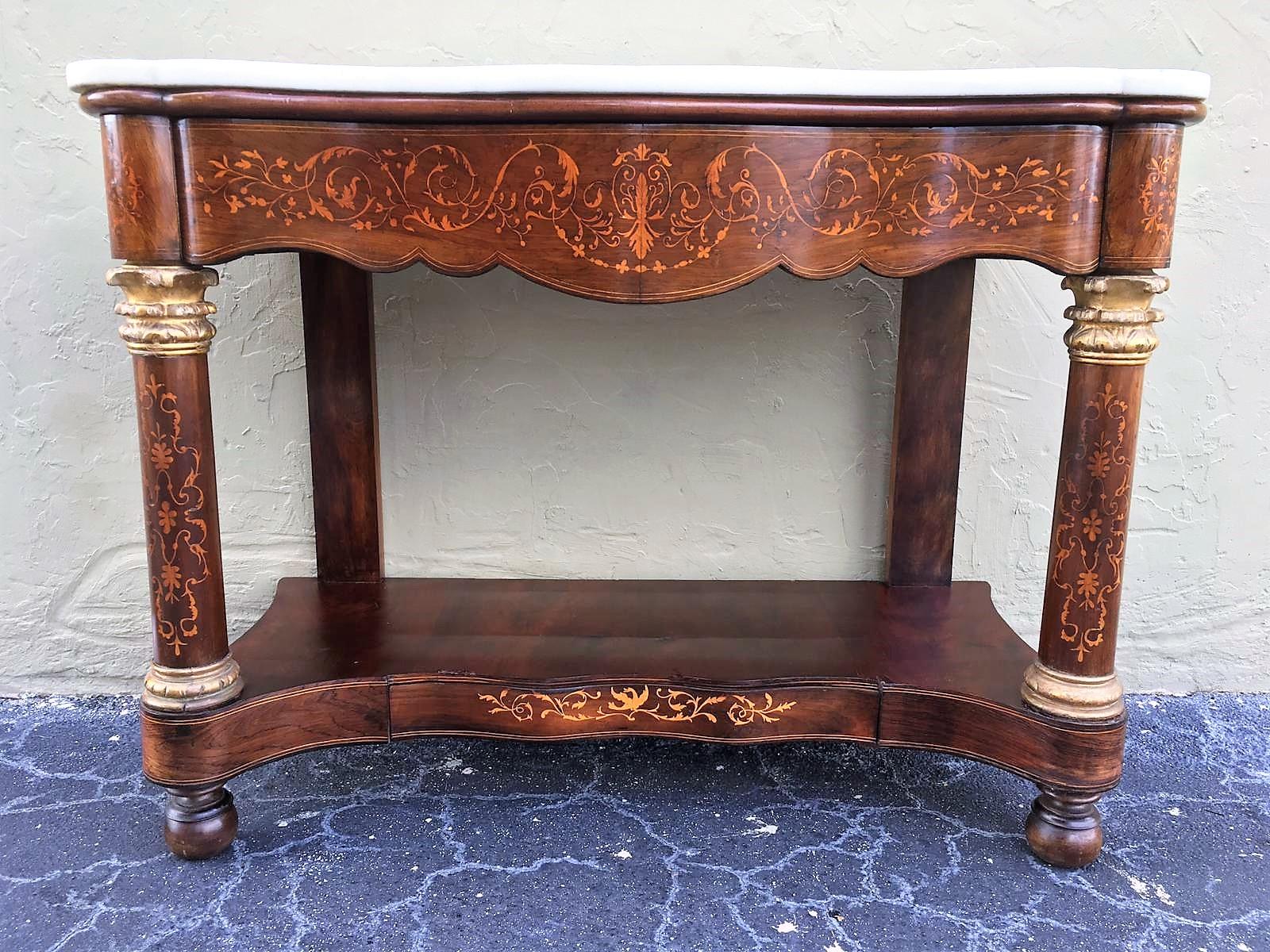 Early 19th century console in wood veneer with a white marble top. It features beautiful marquetry of rinceaux and floral motifs. It is resting on two straight legs in the back and two front columns legs. The console is set on a large base with one