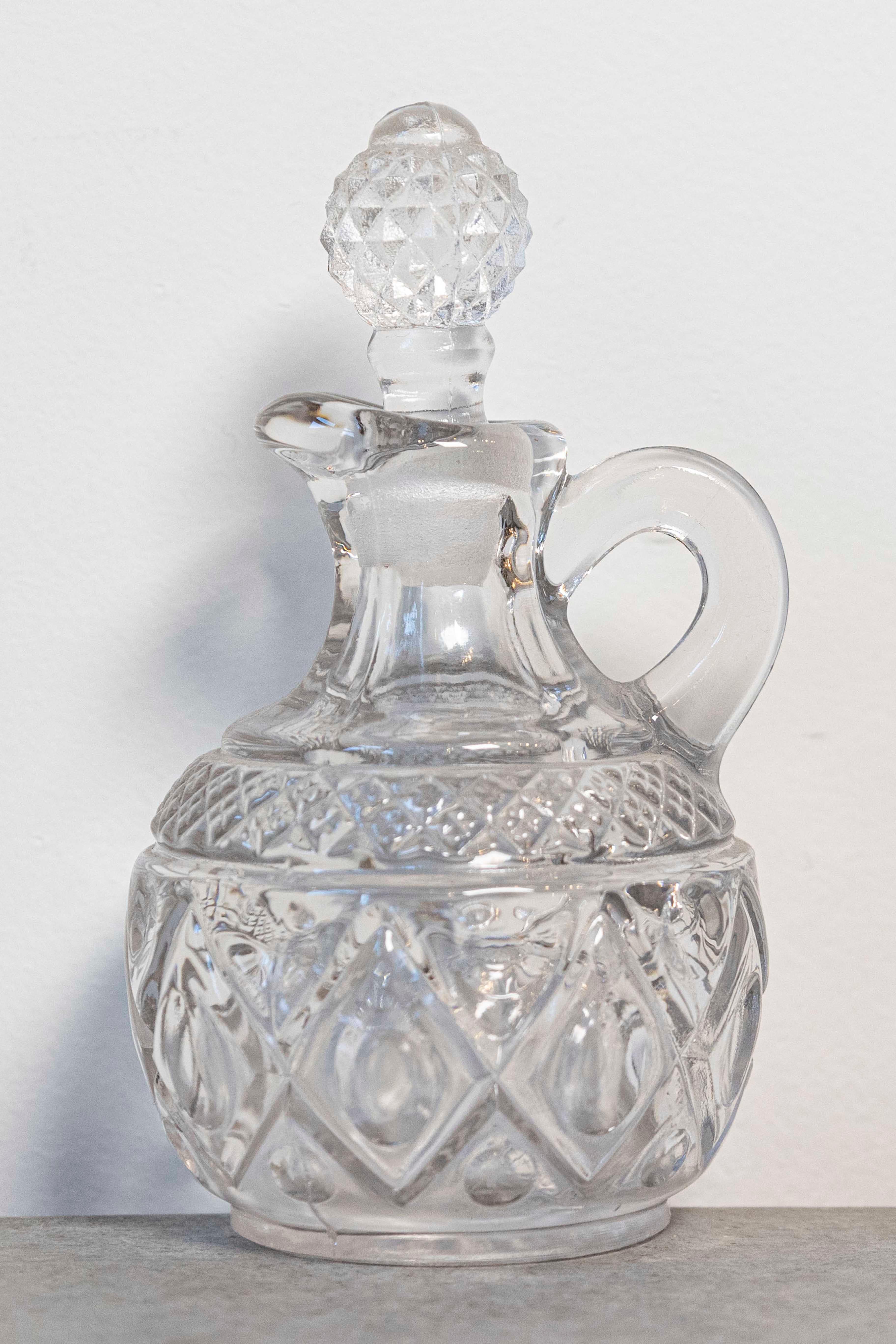 Cette exquise cruche à huile d'olive miniature en verre taillé du 20e siècle est une pièce charmante et fonctionnelle qui témoigne de l'élégance de l'artisanat du verre. Le pichet est orné d'un magnifique motif en forme de diamant qui entoure le