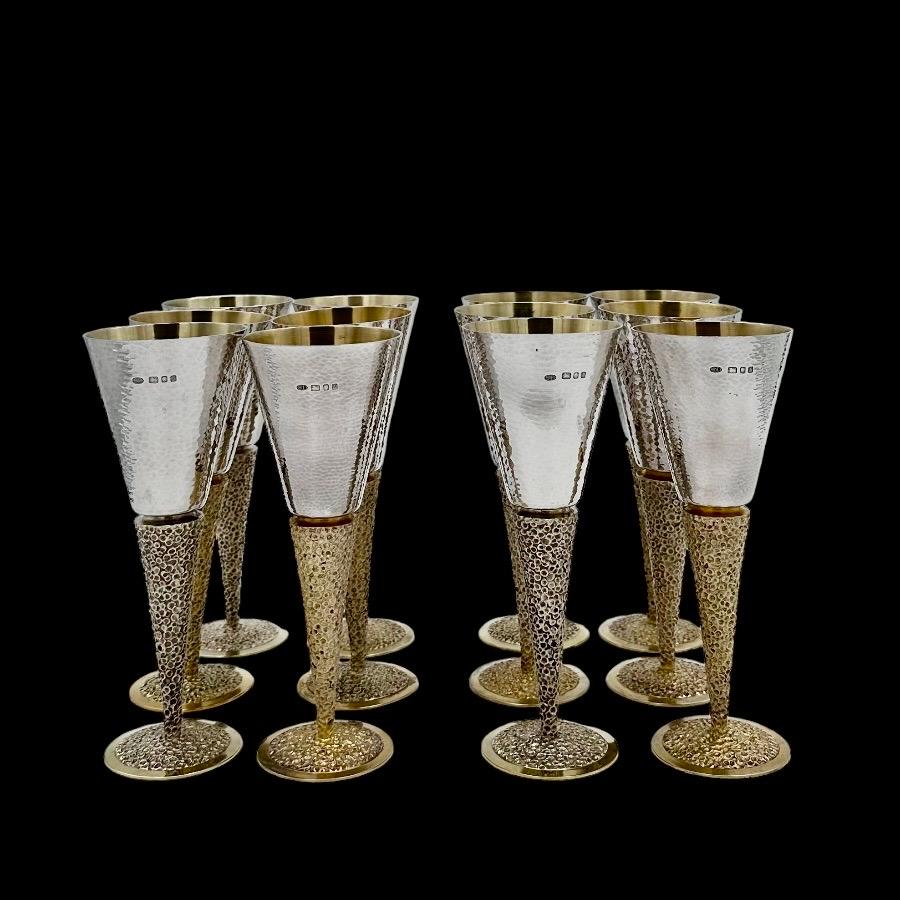 An Impressive suite of 12 sterling silver champagne flutes designed with vase shaped bowls and styled with beautiful hammered patinas.  The silver gilt raised pedestal feet have elegant bark effect decoration for lowlights.
The silversmith Stuart