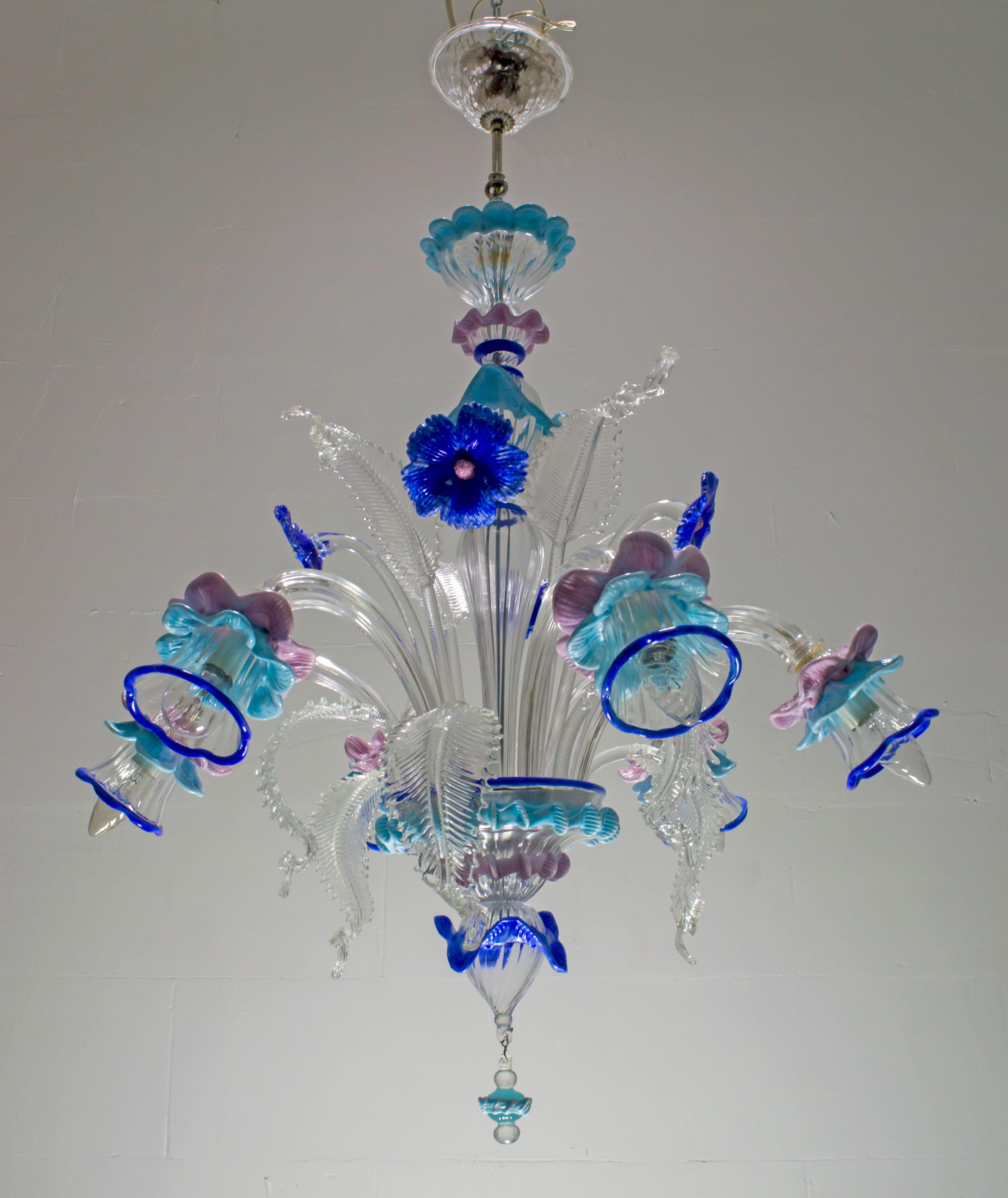 Elegant chandelier with six lights in Murano glass of transparent color and sophisticated finishes in blue, turquoise and antique pink. With a centered bulbous column that emits branches and flowers and finely cuts the Murano glass
