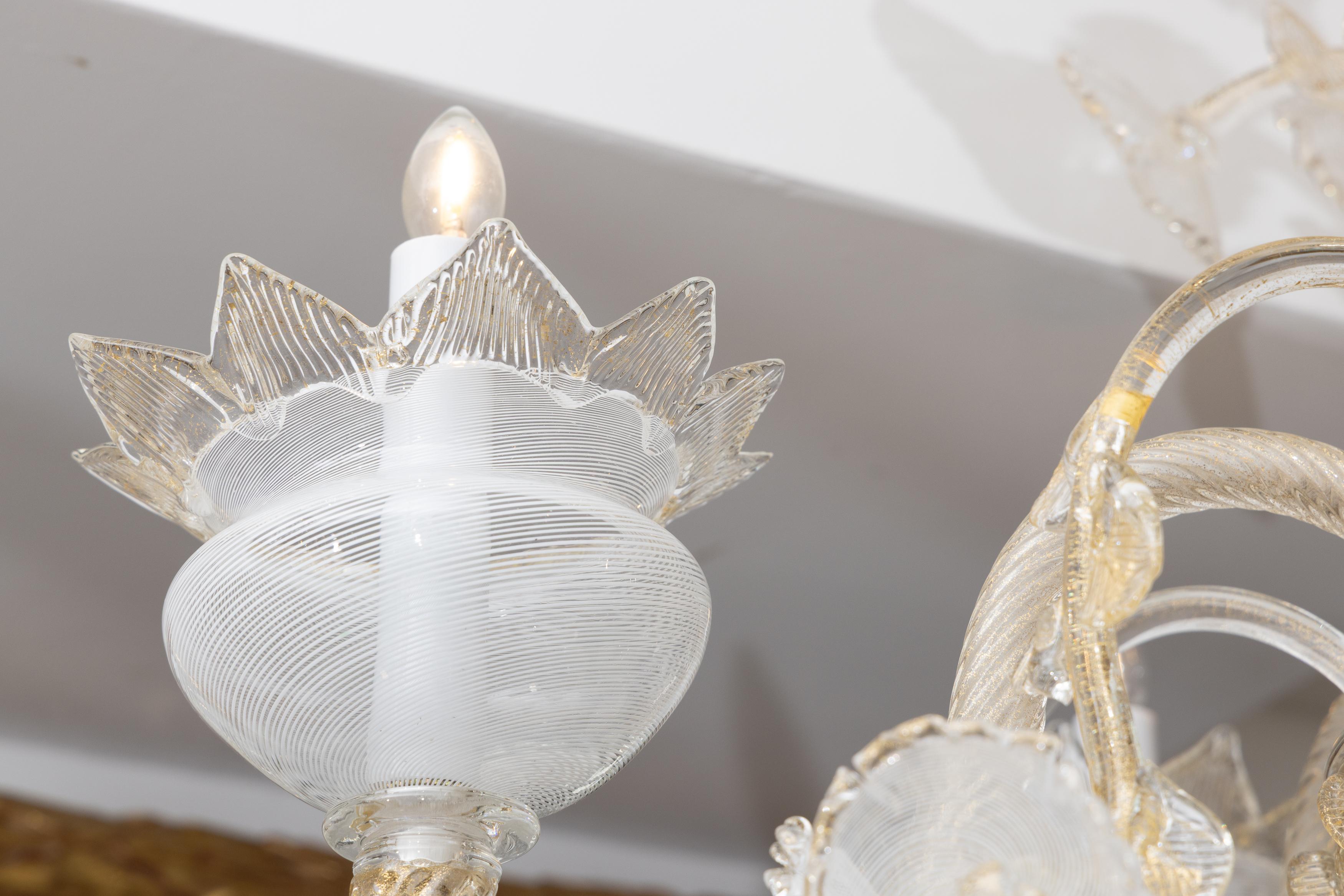 Il s'agit d'un ravissant lustre de Murano, dont le verre clair soufflé à la bouche se marie à l'or, créant ainsi une présentation élégante.  Le lustre est composé de cinq bras en verre tourbillonnant et d'un bouquet central de fleurs à longues