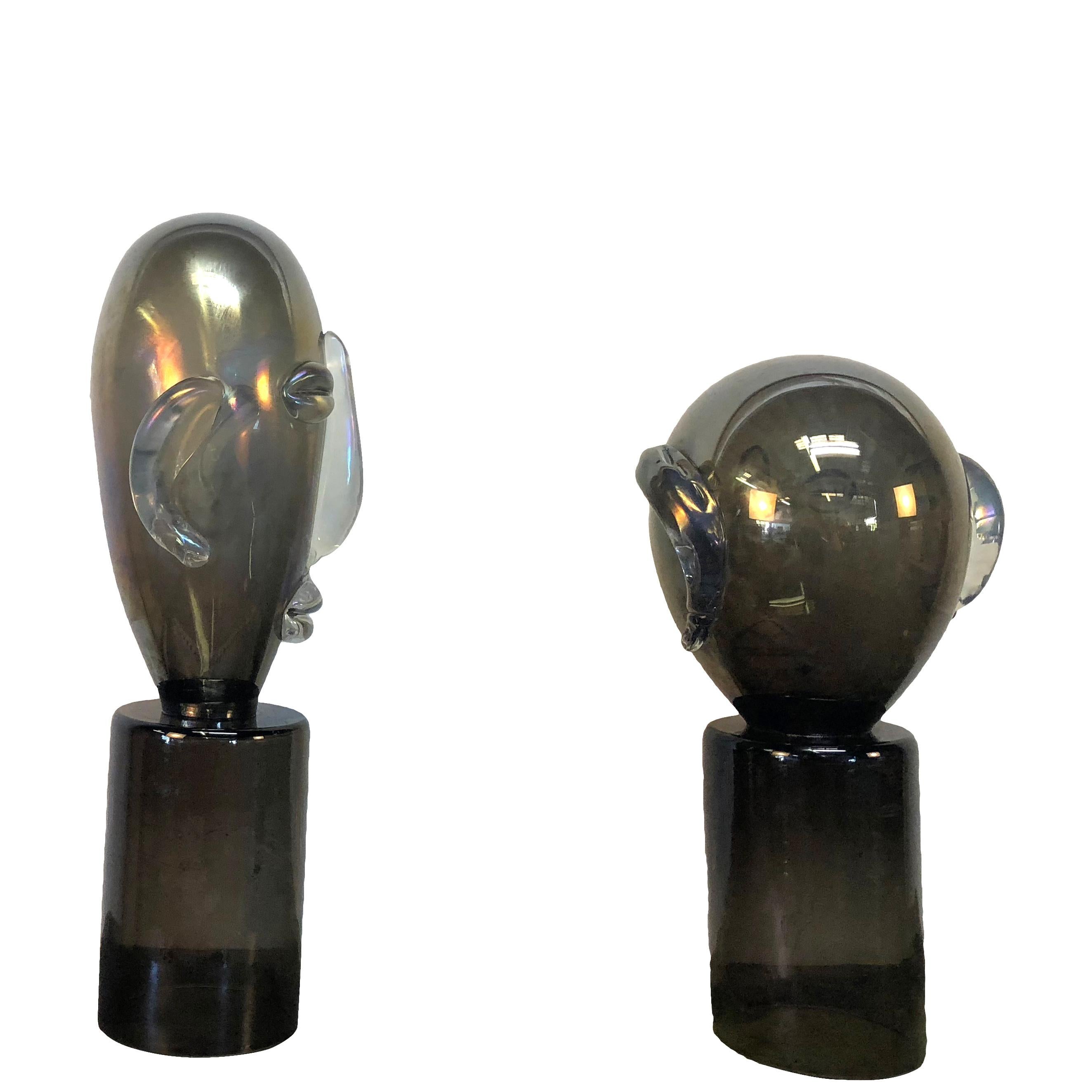 A dark-grey, black vintage Mid-Century Modern Italian pair of Murano glass head ornament set on a round base in the manner of Pablo Picasso. In good condition created in hand blown glass with iridescent highlights. Wear consistent with age and use.