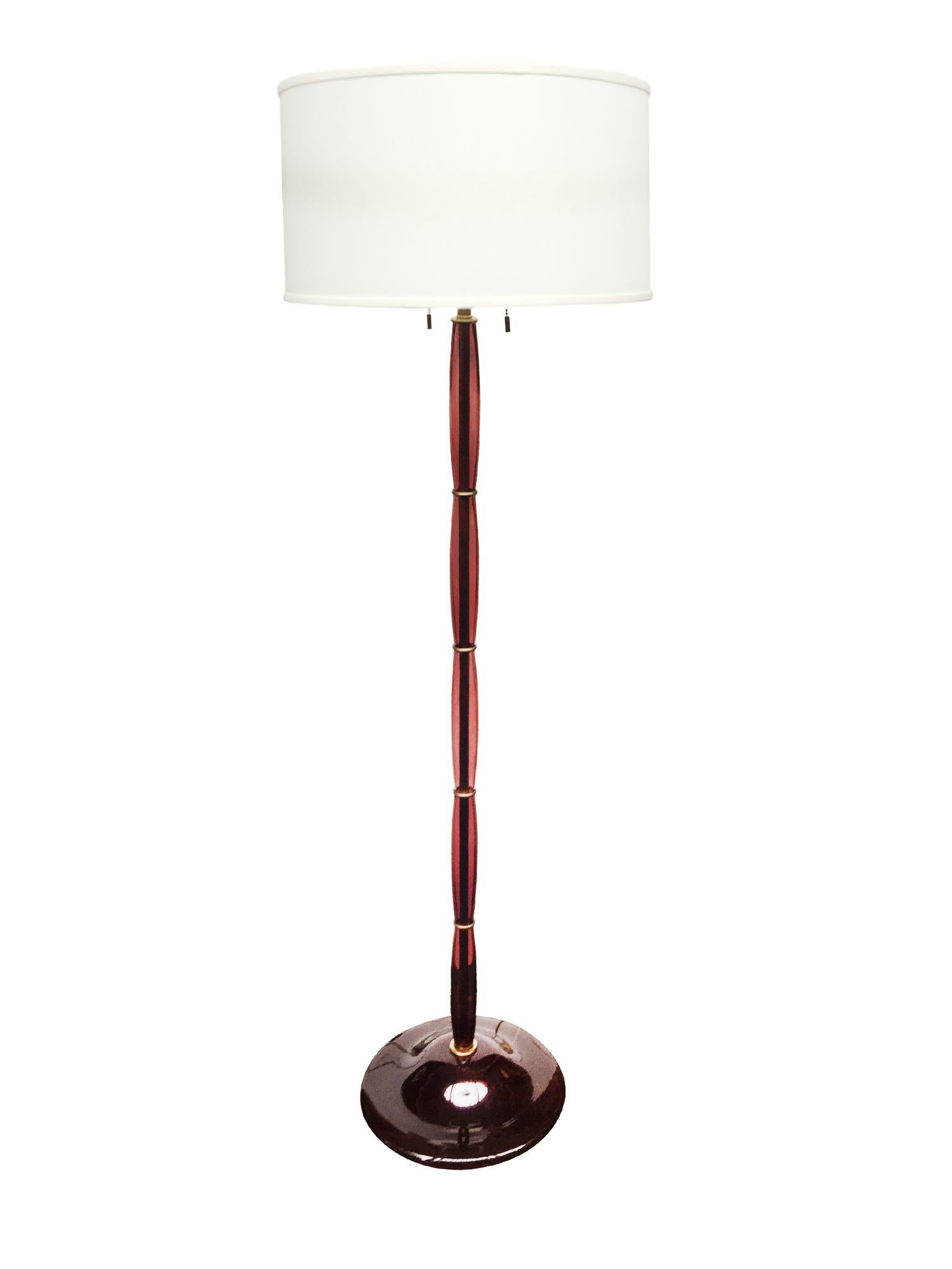 This stunning floor lamp offers a translucent note of color and lighting. It is comprised of handblown Murano glass in a rich plum hue. The design is an elegant tower of spindle forms supported by a bell-shaped base, also in glass. Brass rings