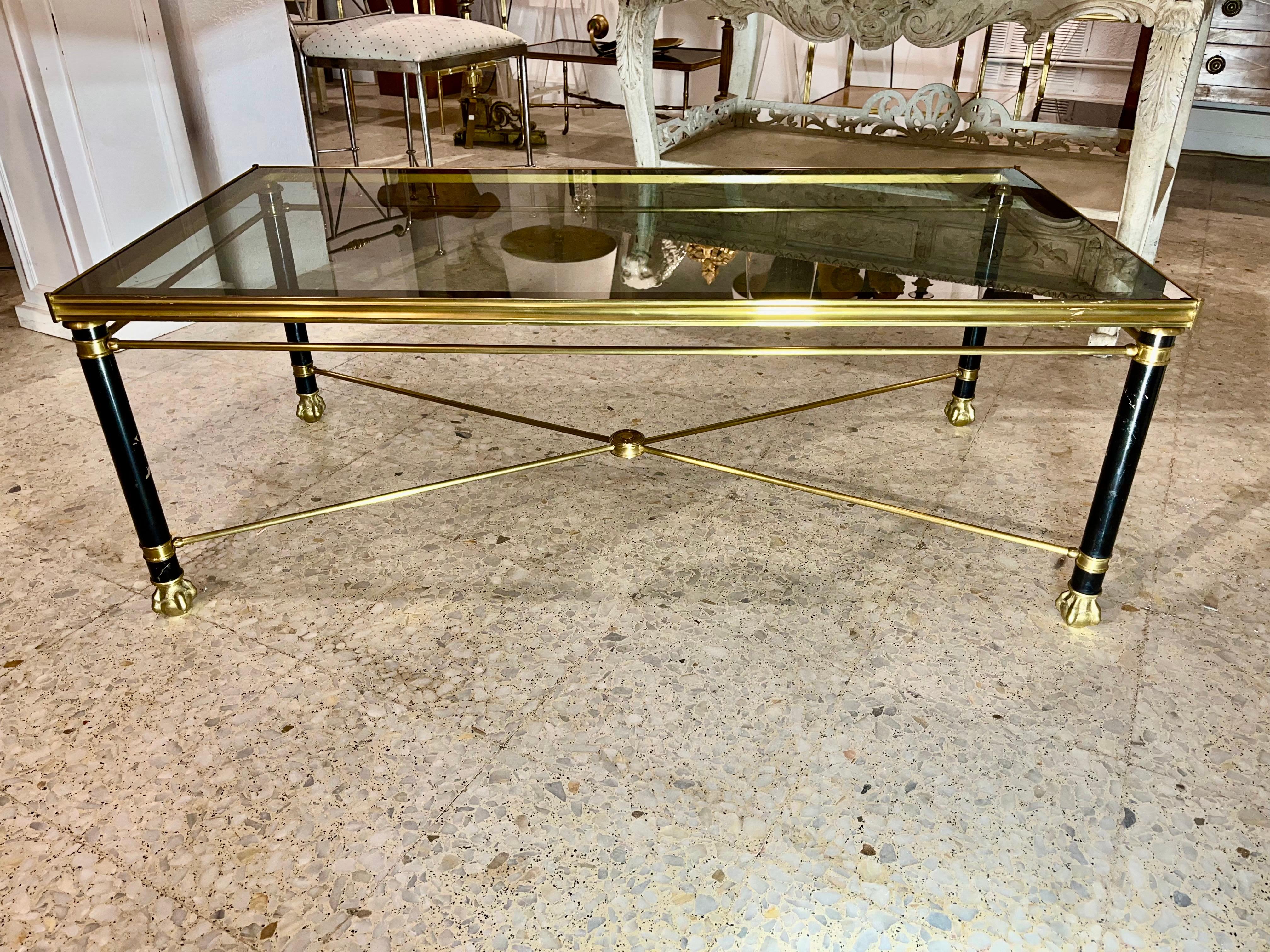 An elegant coffee table or center table in the style of Maison Jansen, in neoclassical style combining black lacquered metal for the side legs with gold brass that holds a gray glass framed in a darker tone, the legs rest on animal claws and have an