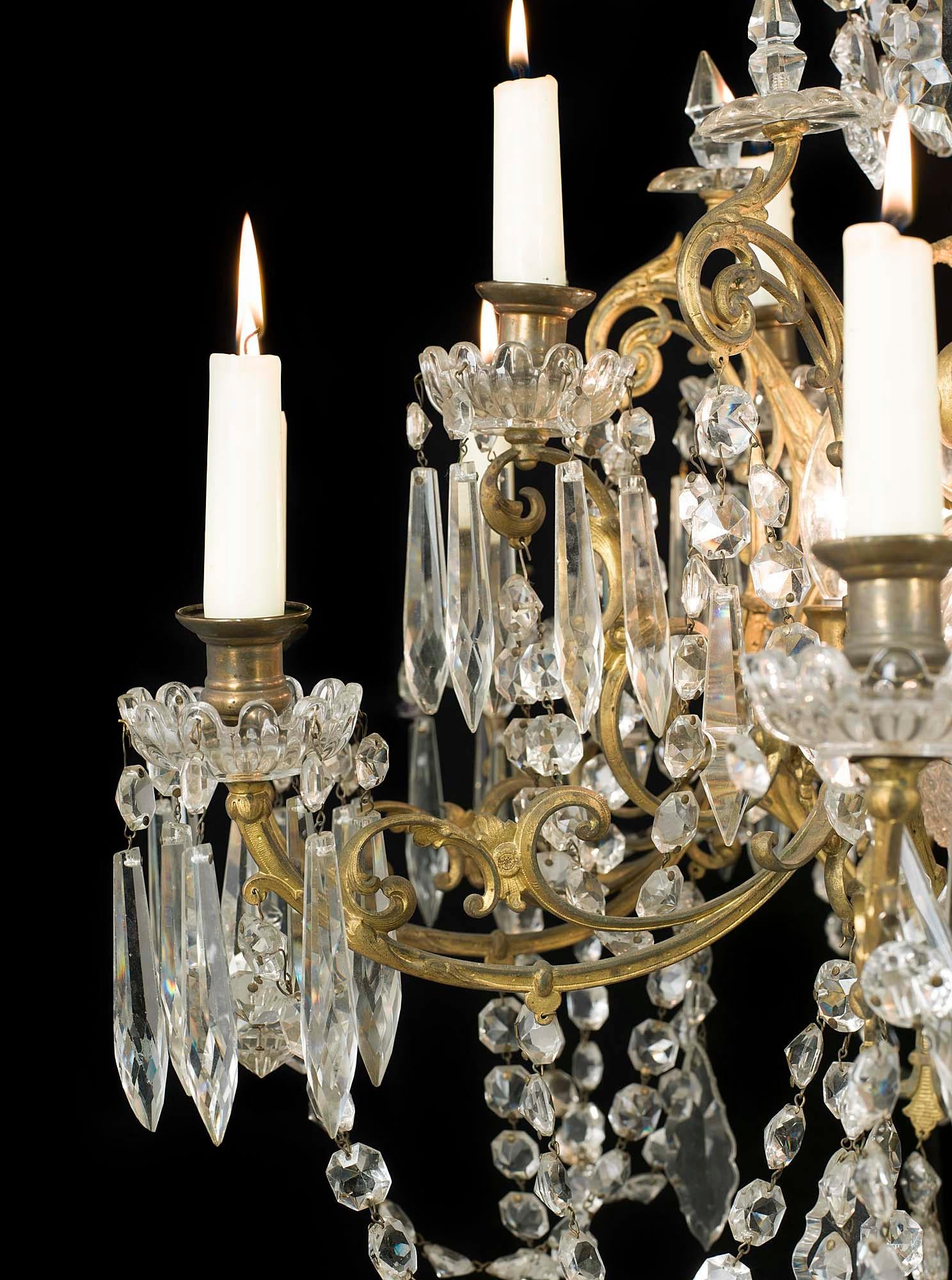 An early 20th century cut-glass and gilt metal neoclassical style fifteen candle chandelier in two tiers with glass drip trays and swags set on a gilt metal scrolling frame. The candles are not wired for electricity but there are five light bulbs