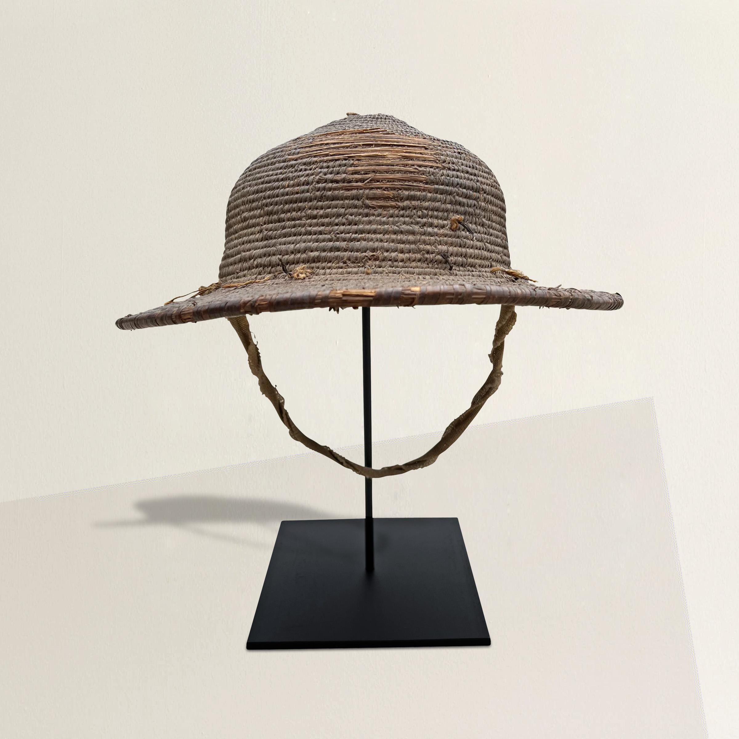 A wonderful mid-20th century Nigerian woven fiber hat with a wide brim, chin strap, and mounted on a custom steel mount.