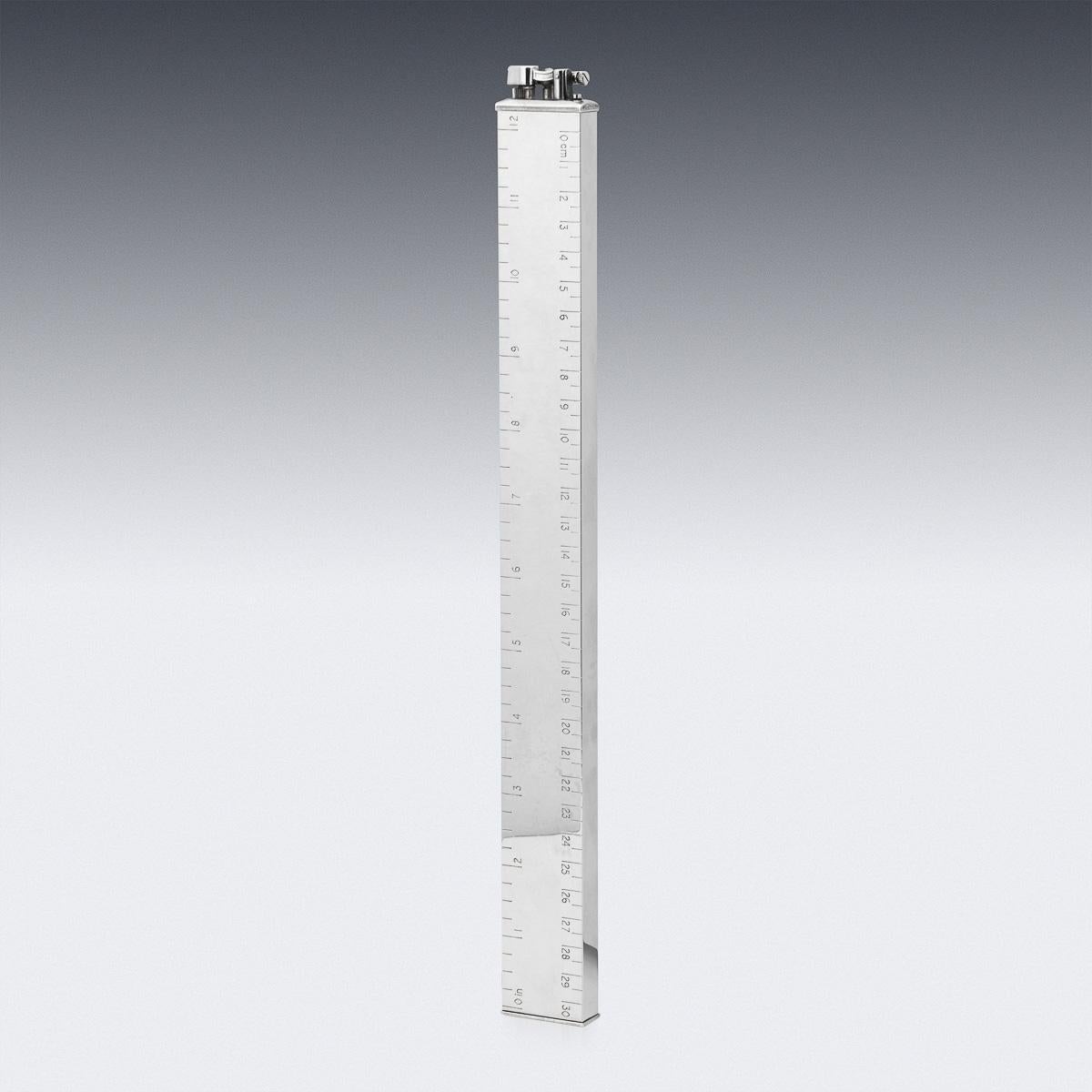 Un accendino da tavolo estremamente elegante del XX secolo, placcato in argento, che ha la forma di un righello da 12 pollici calibrato sia in pollici che in centimetri. Marcato Dunhill, Made in England. 

Alfred Dunhill Limited è stata sviluppata