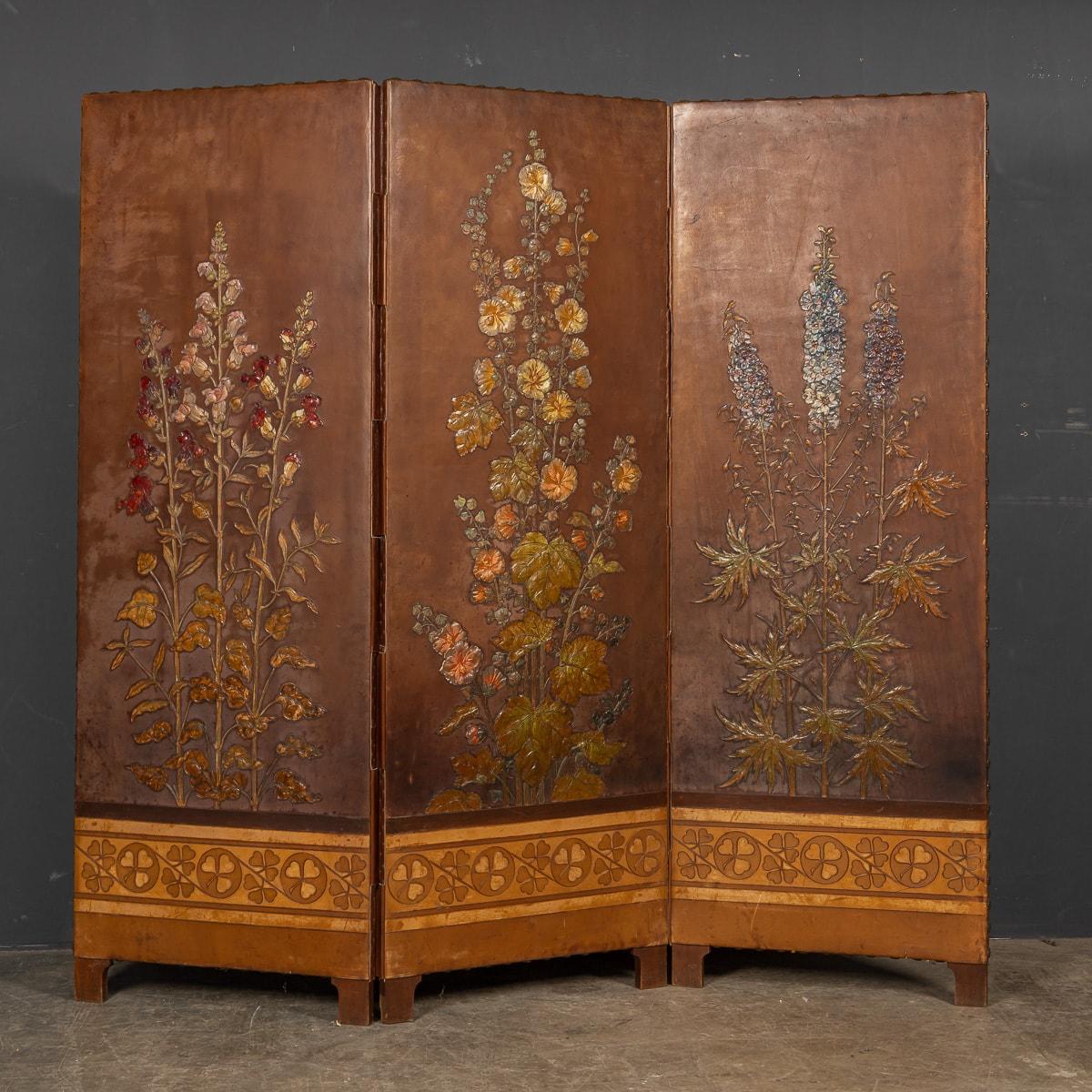 Antique early 20th Century Arts & Crafts three panelled leather screen, beautifully embossed, oil painted with hollyhocks delphiniums and foxgloves. Along with a stylised border along the bottom and brass stud work around each panel. This piece is