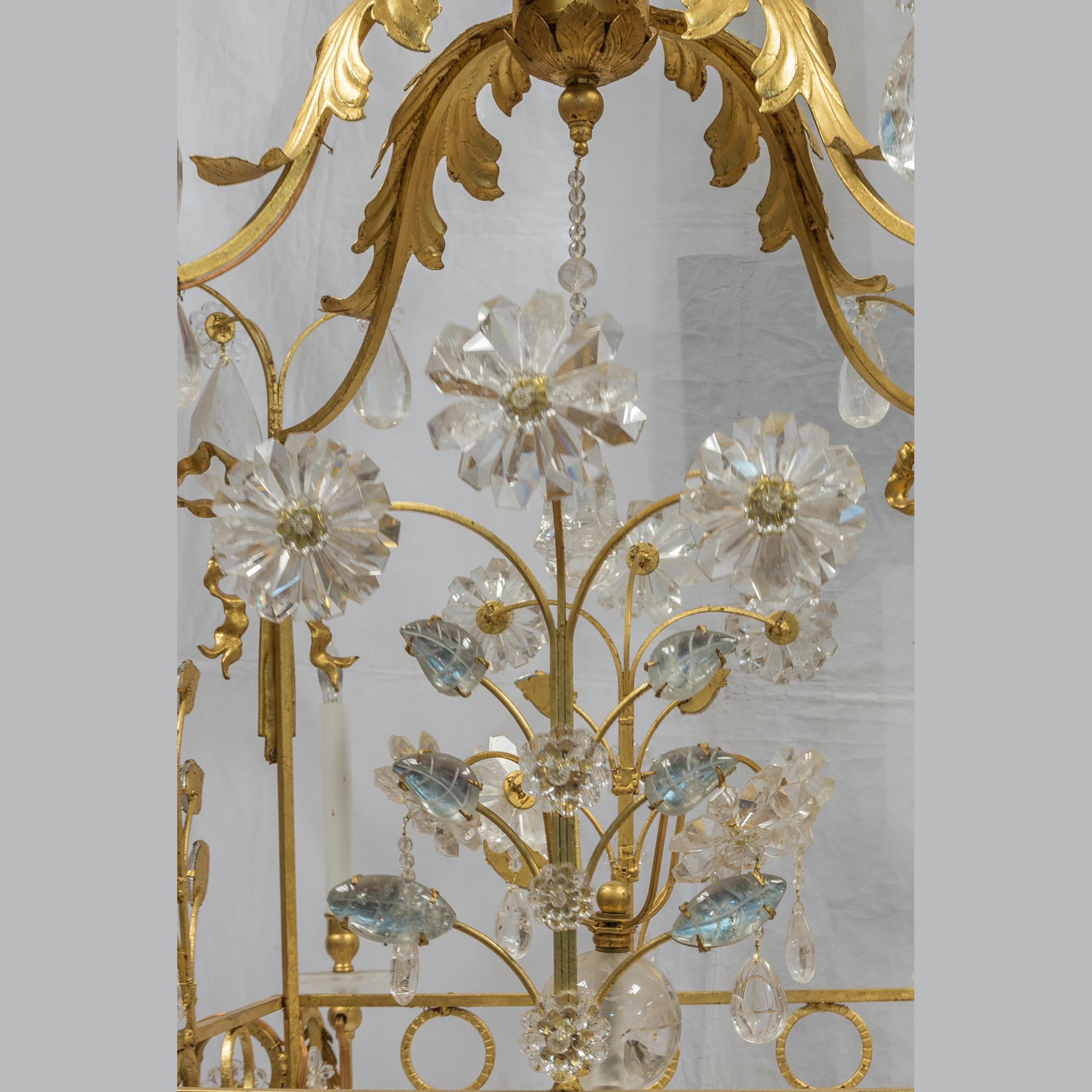 20th Century charming gilt-metal and rock crystal cage-formed eight-light chandelier mounted with multifaceted hand carved rock crystal center column and profusely mounted with rock crystal elements and drops on branches. Gilded bronze foliage and