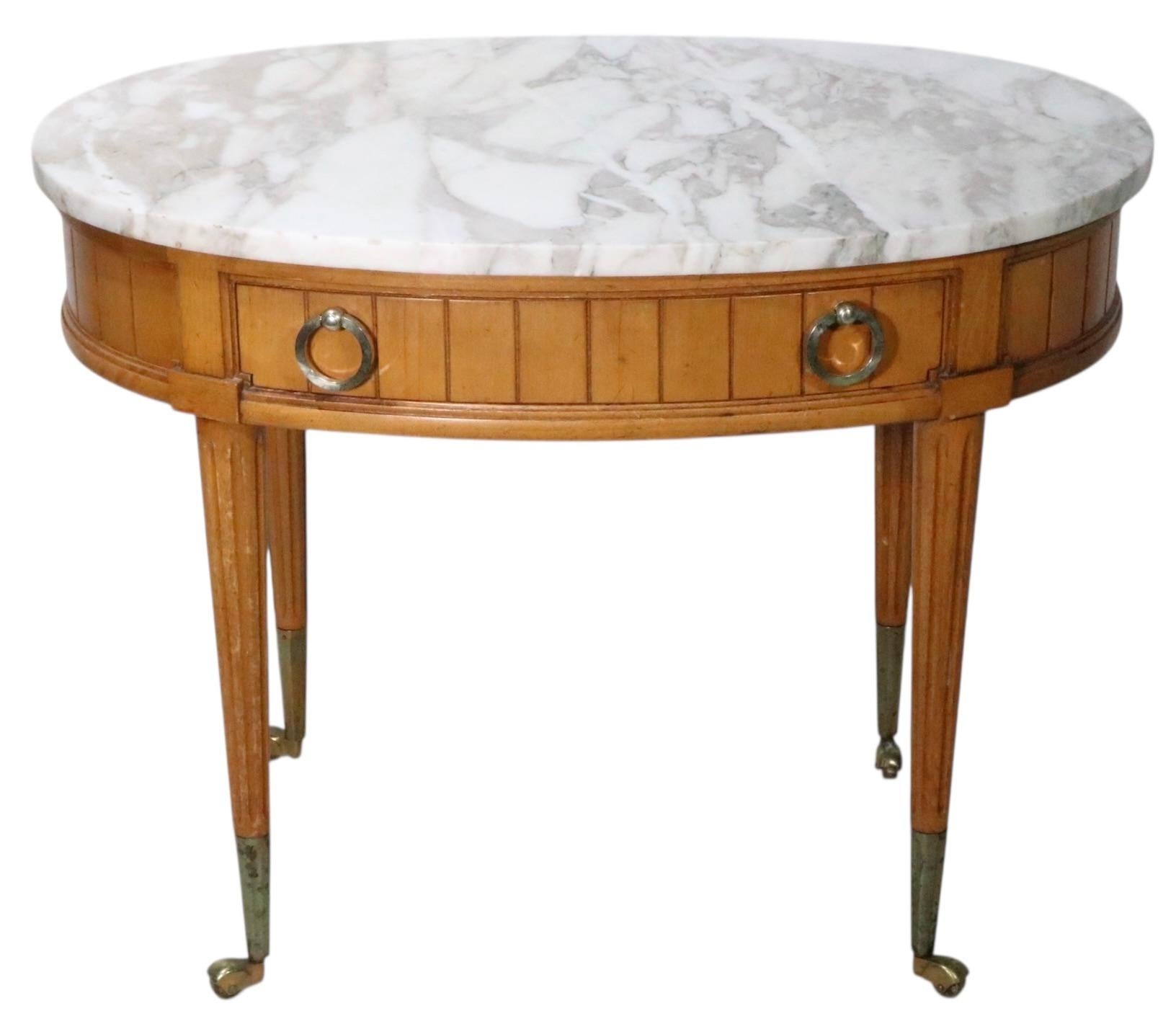 Mesa decorativa vintage con tapa de mármol a la manera de Luis XVI, hacia 1950/60. El soporte tiene una gruesa encimera ovalada de mármol, apoyada en una base de madera de un cajón. Probablemente fabricada en Italia, de estilo francés, sin firmar.