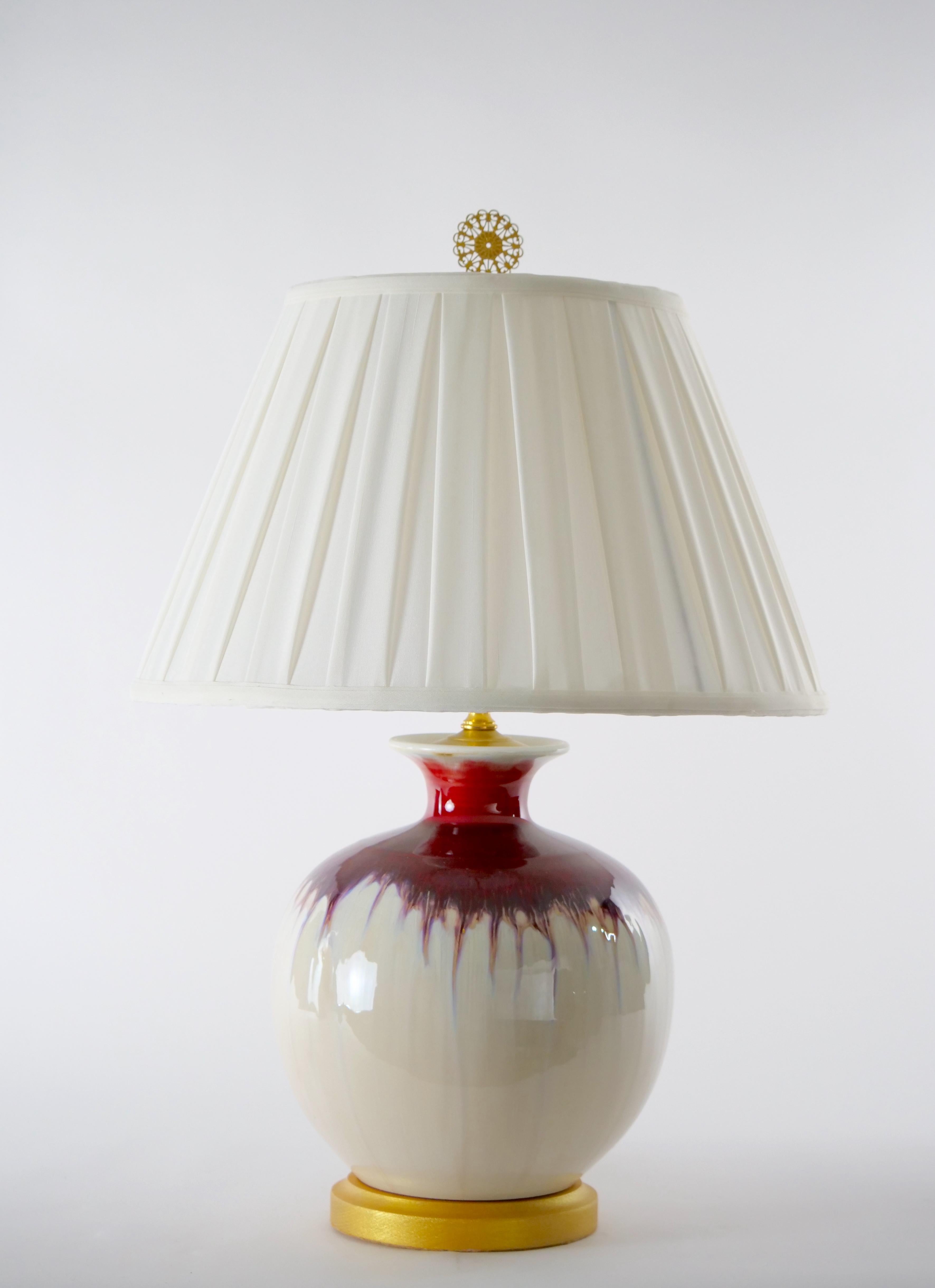 20th century flambe porcelain bottle shape vase table lamp with gilt wood base. Each lamp features a bright red and beige glaze color in a bottle shape form with flared neck , resting on a round gilt wooden base. Each one is in great working