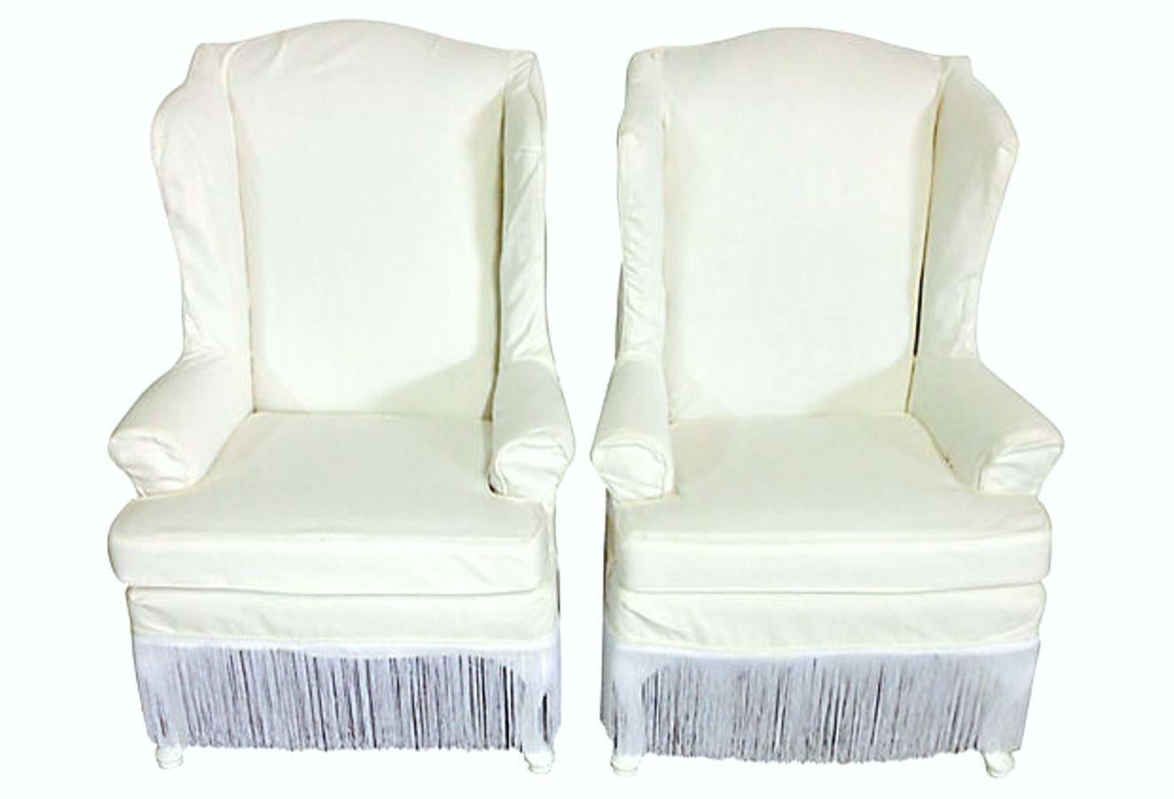 20th Century Pair Of American Queen Anne Style Wood Frame Upholstered Slip Cover Wing Back Arm Chairs. Features the original upholstery fabric in tact with newly made white denim and satin fringe detail slip covers. The mahogany legs are lacquered