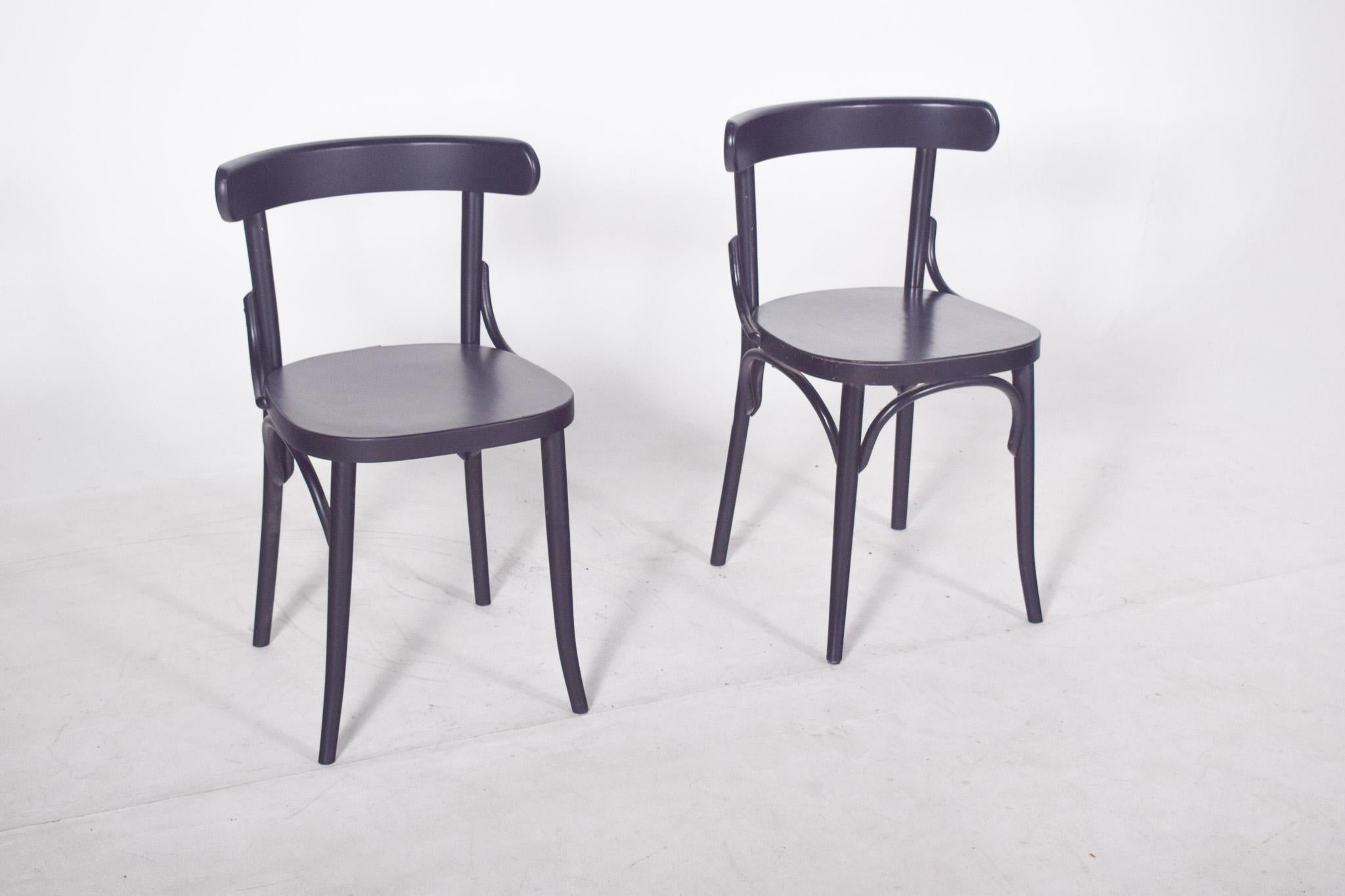 Paire de chaises peintes en noir avec un dossier bas et incurvé qui se prolonge latéralement en une ligne continue et lisse, caractéristique du design fonctionnaliste du 20e siècle. La structure présente des formes simples et discrètement incurvées,