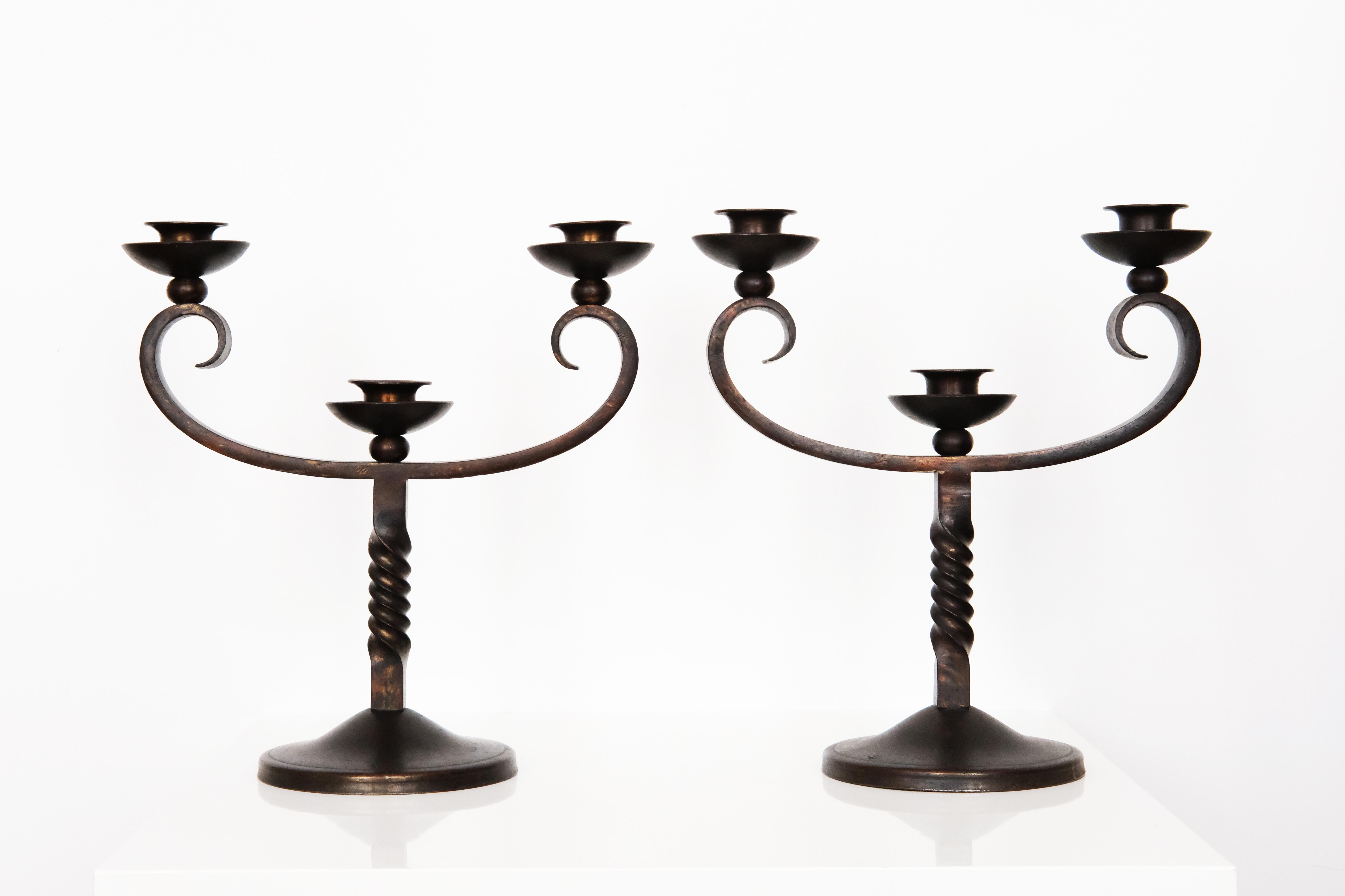 Questa bellissima coppia di portacandele dell'inizio del XX secolo, firmata Charles Piguet, è realizzata in ferro battuto e mostra una sofisticata miscela di arte e artigianato. Il design di ogni pezzo è dinamico ed elegante, con tre graziosi bracci