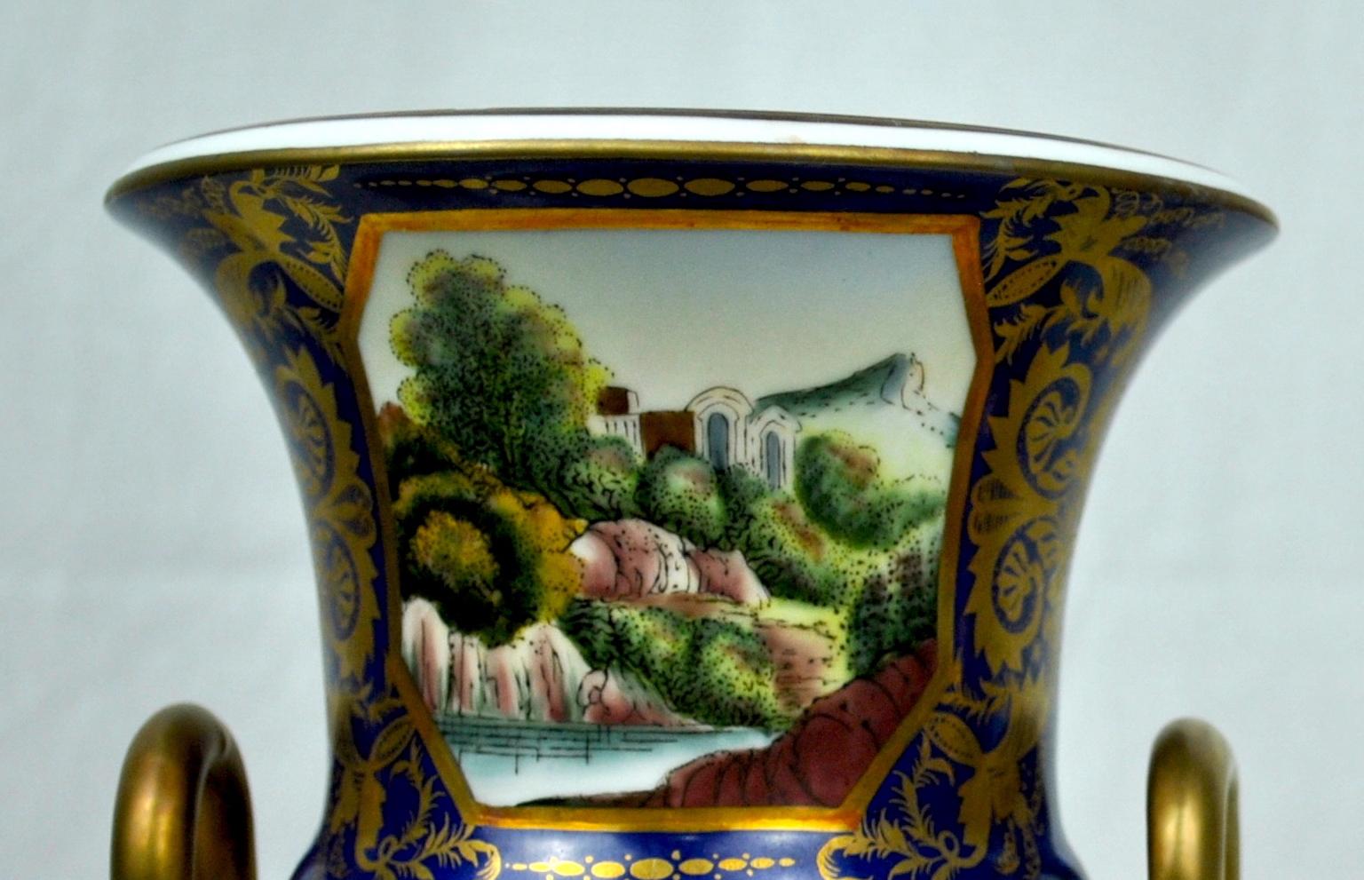 A 20th century pair of deep blue and gold hand painted guilt sieve vases with painted landscape scenes and guilt serpentine snake handles.
