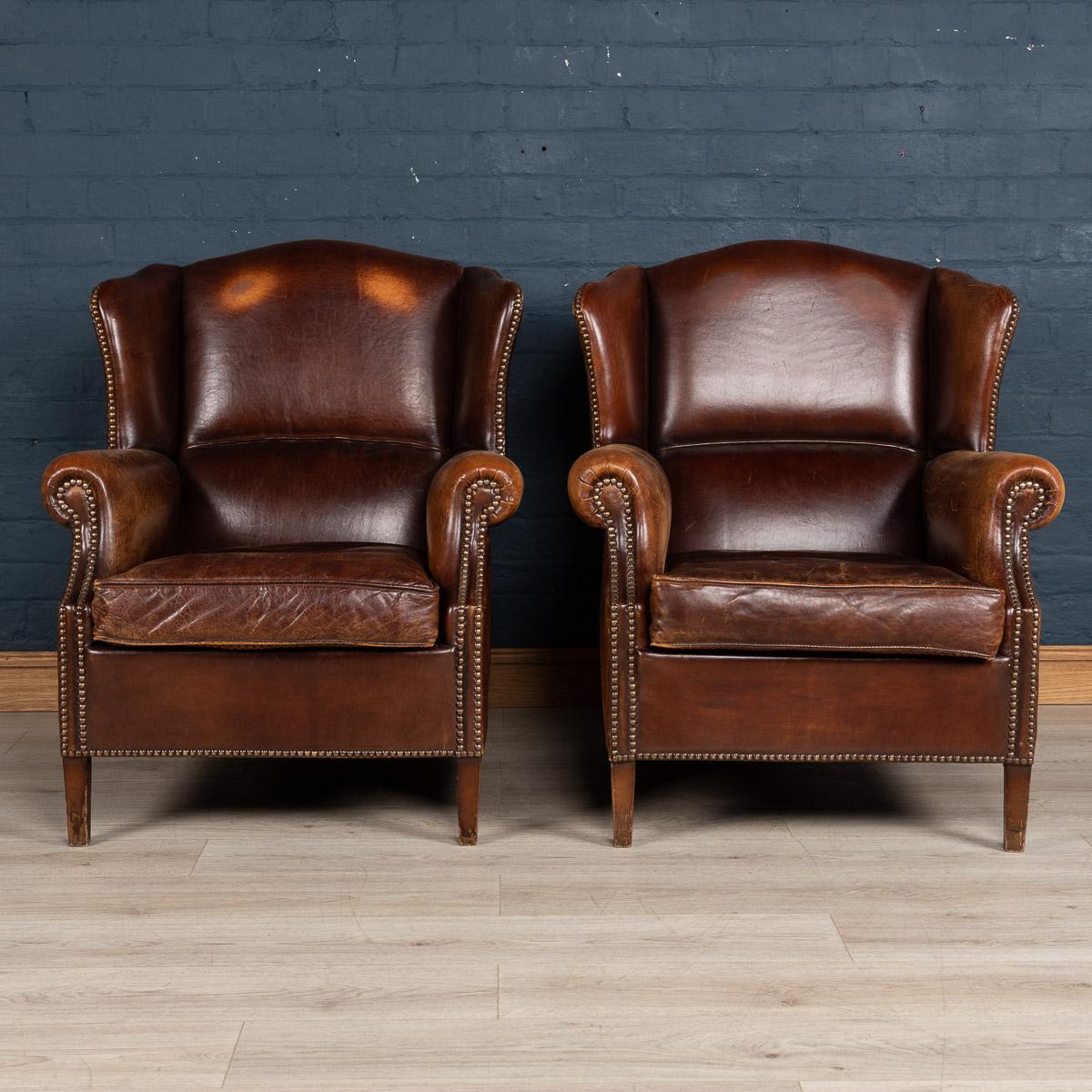 A wonderful pair of leather wing back armchairs. Dating to the late 20th century these chairs were realised by the finest Dutch craftsmen, the solid wood frame upholstered in superb quality leather which over the years have only gained in class and