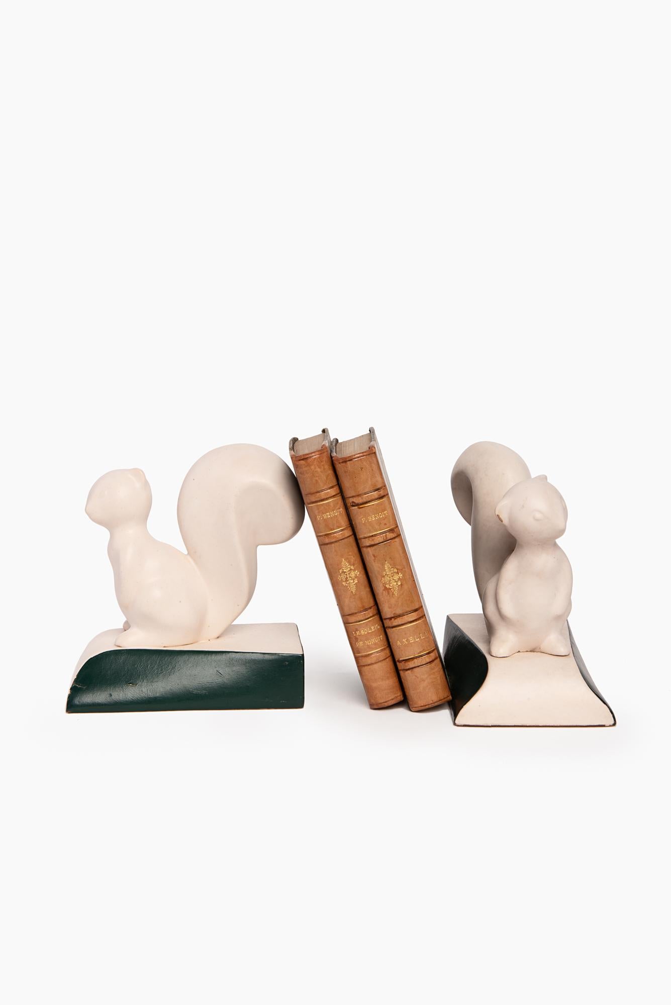 Lovely pair of French Art Deco style bookends; two stylized squirrels in fine white porcelain are depicted; the base is covered with very dark green leather to create a nice contrast with the rest of the object; overall the design is light and