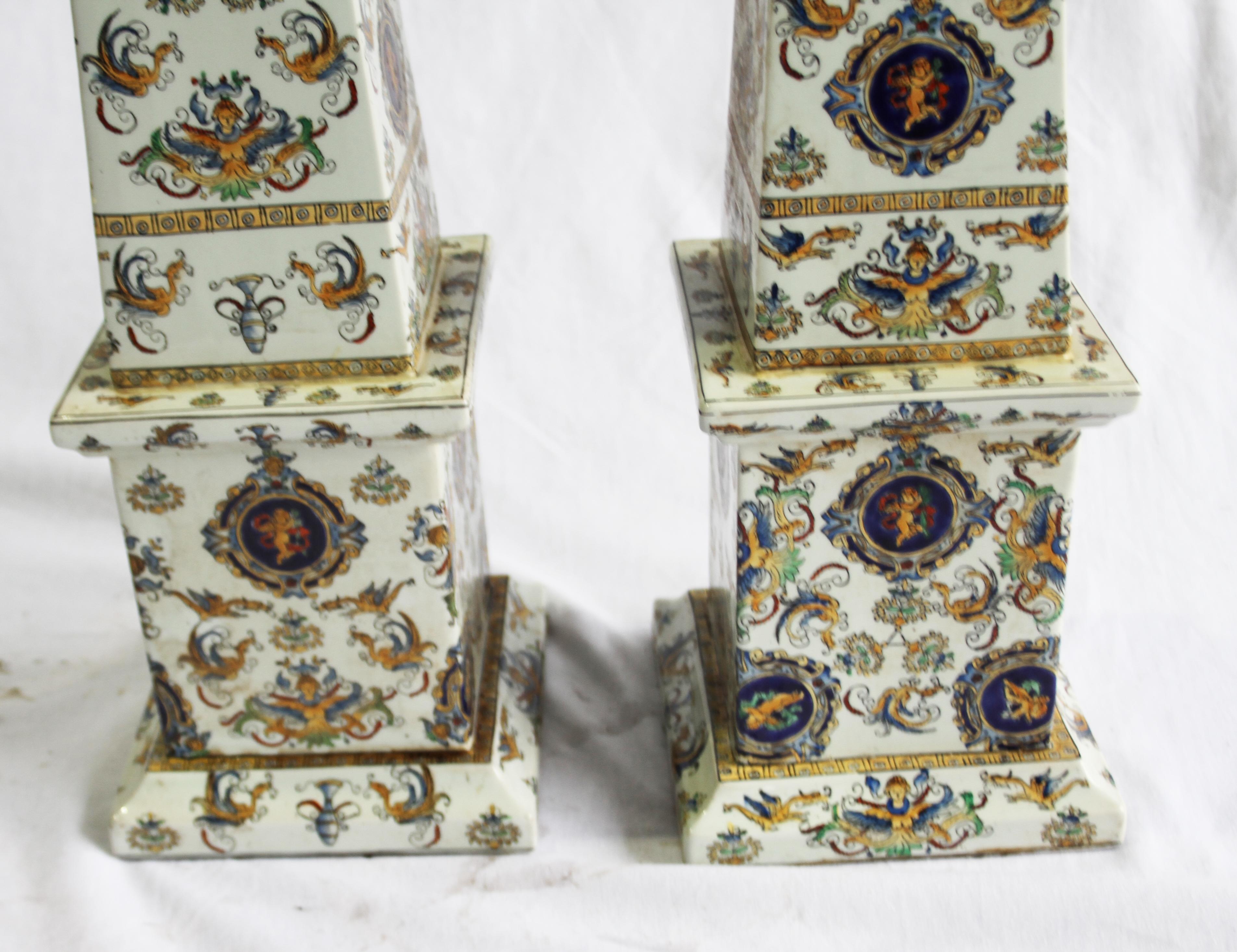 Pair of highly decorative, hand painted porcelain obelisks. 

Wonderful vibrant color decoration with cherubs on plaques.