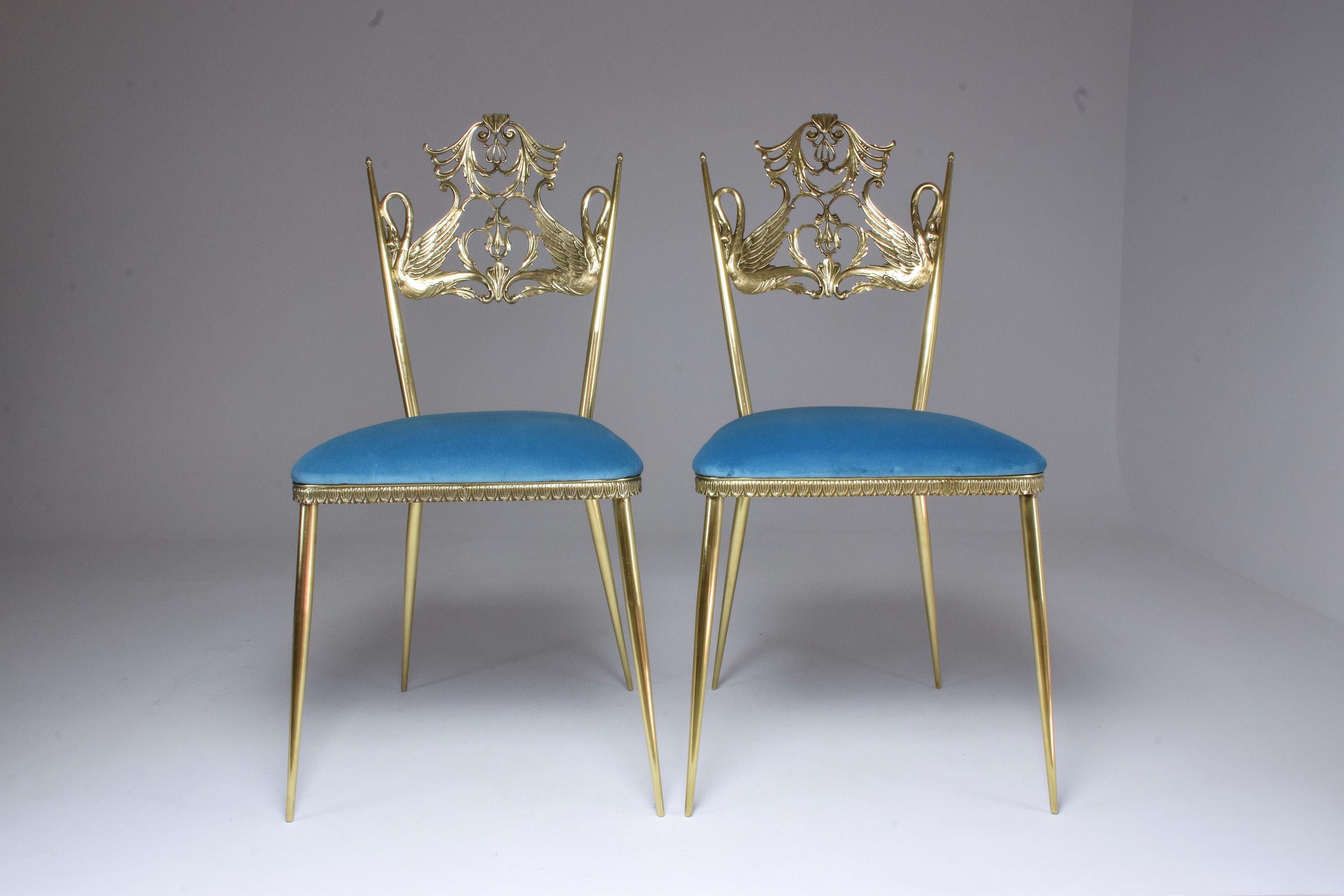 A set of two mid-century accent or side statement chairs designed in a solid gold brass structure with two sculpted swan birds in fully restored condition through careful polishing, new foam padding, and light blue reupholstered velvet