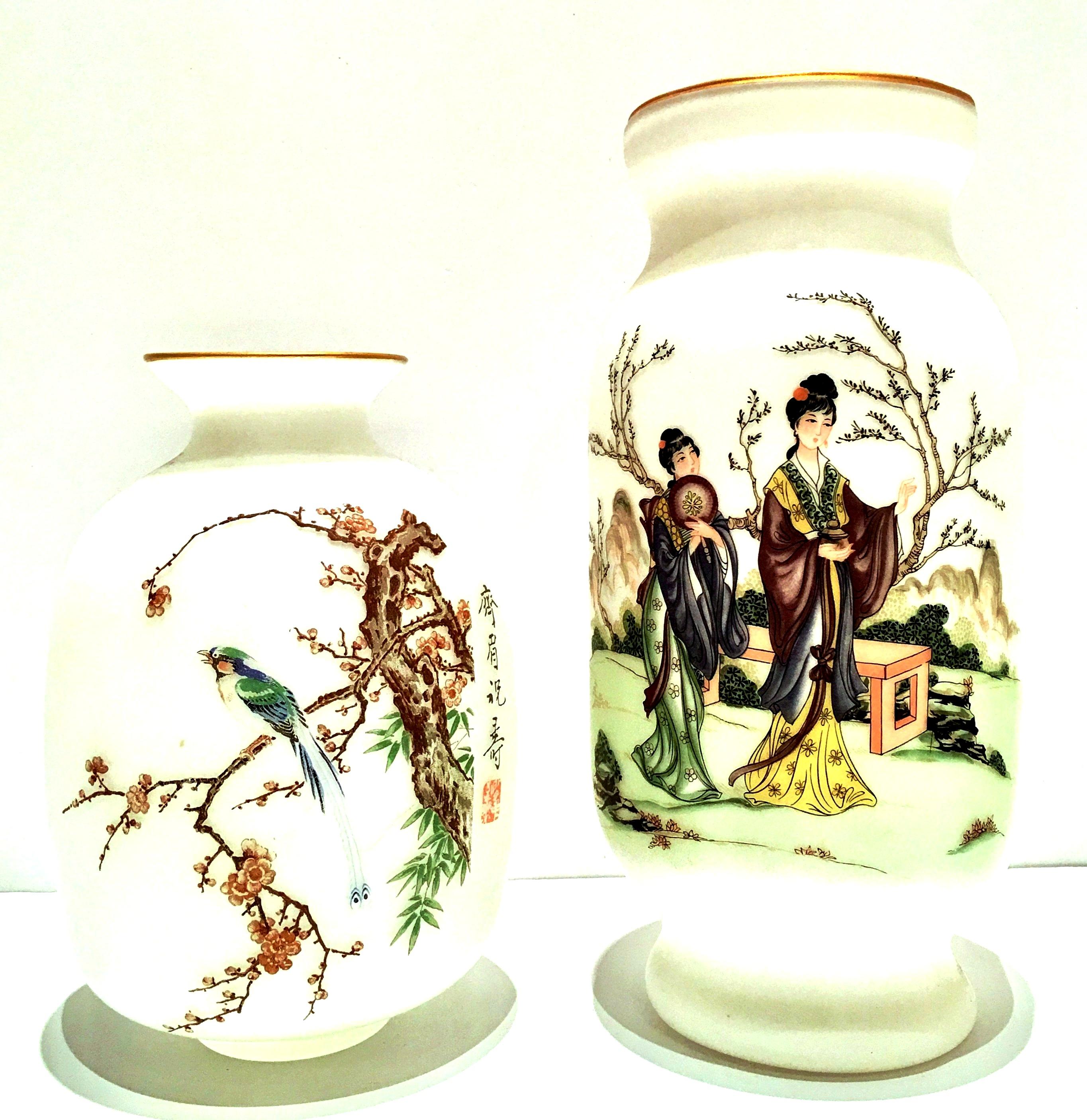 Mid-Century Pair Of Japanese gilded gold rim hand-painted satin glass vases.The larger vase features two Geisha girls walking by a park bench with fans in their hands. The smaller vase has a Classic cherry blossom tree and bird motif. Each one is