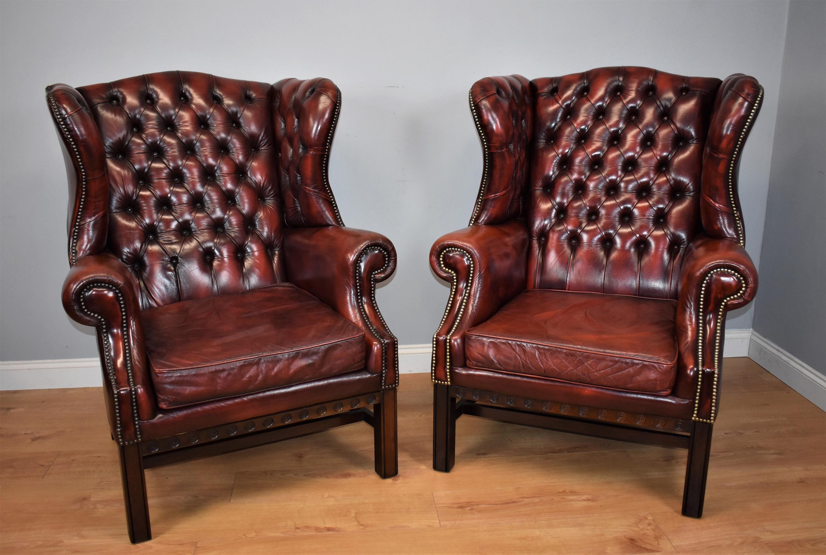 For sale is a good quality pair of red leather wingback armchairs of exceptionally large size. Each chair has a deep buttoned back and upholster seat, flanked by scroll arms with brass studs. The chairs are raised on square legs united by a single