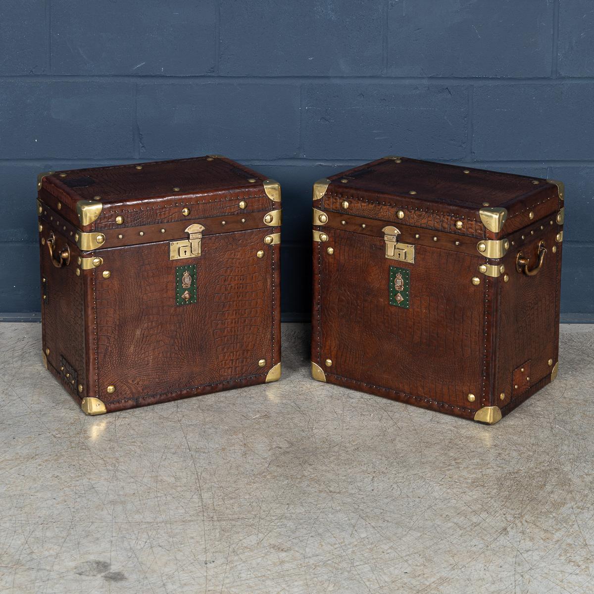 A pair of leather-clad Army and Navy style trunks, crafted in England in the late 20th century, they exude rugged sophistication and timeless appeal. Inspired by traditional military campaign trunks, they feature sturdy leather exteriors with robust
