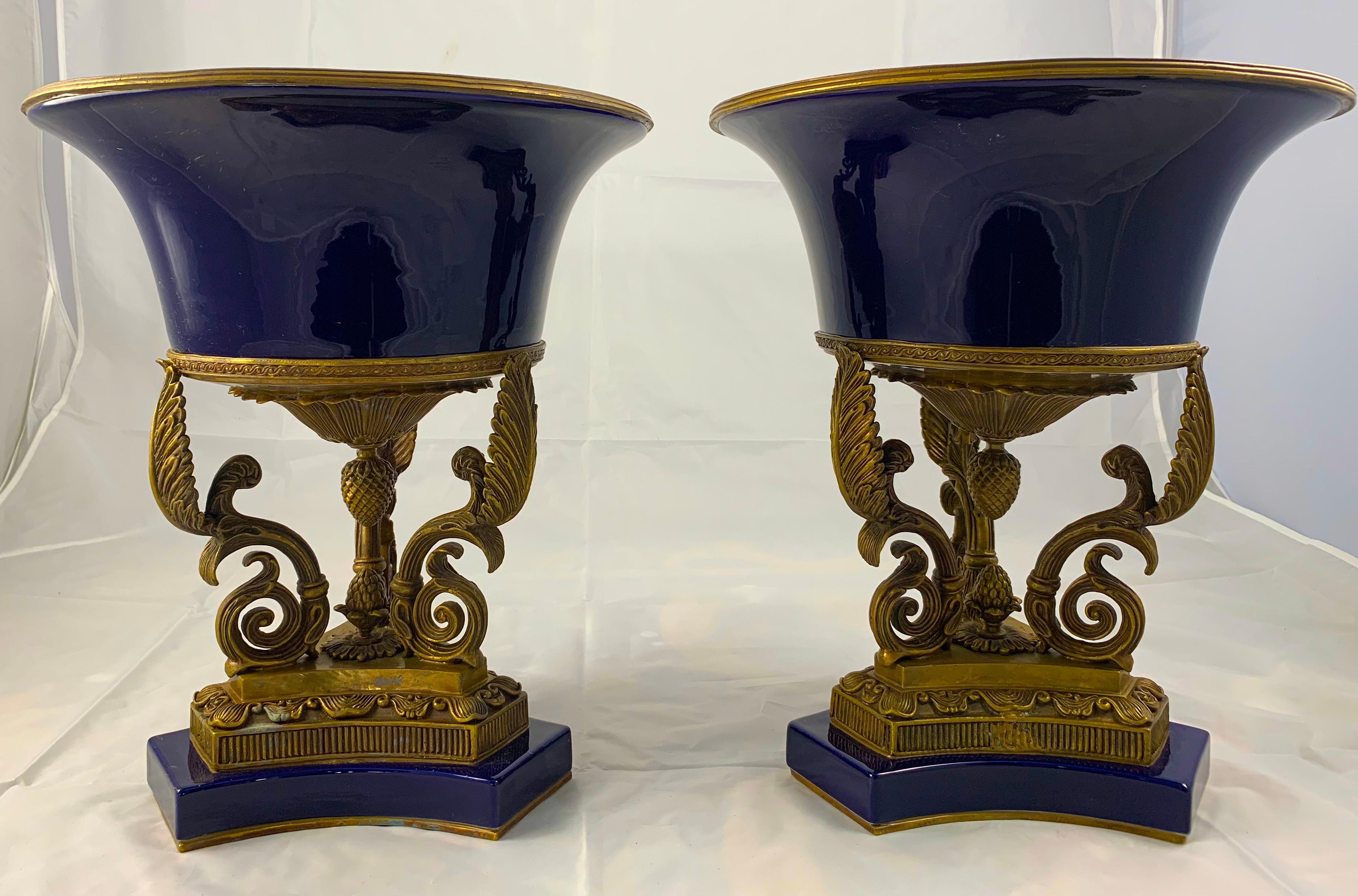 A pair of First Empire style Bleu de roi porcelain and ormolu-mounted urns. Each supported by stylised leafage and scrolls above a tri form base.