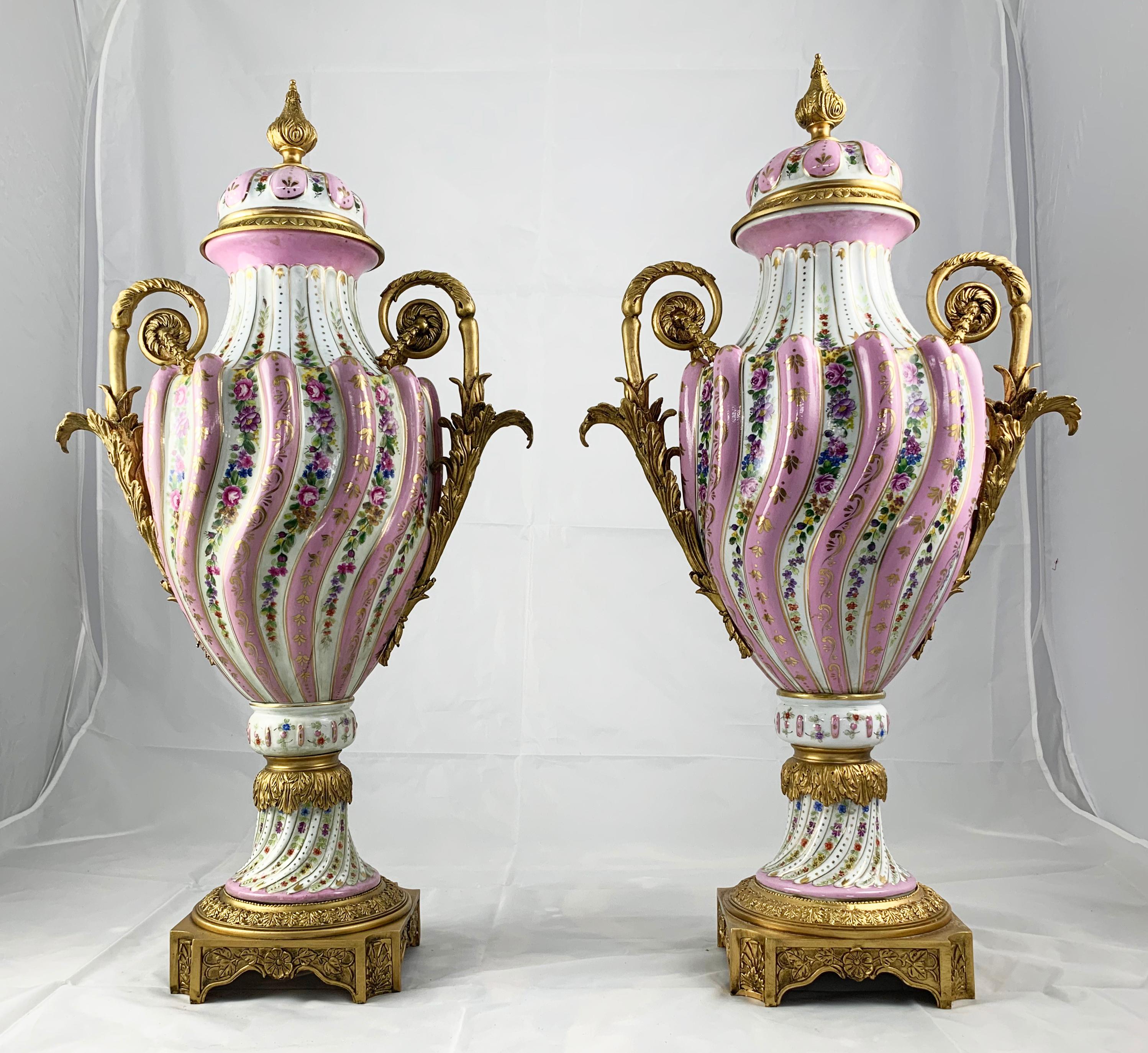 A fine pair of Sevres porcelain two handled vases and covers with ormolu mounts. 19th century. Each with spiral lobed decoration picked out with flowers on a pink ground. The mounts cast with classical motifs. Supported on a shaped square base.