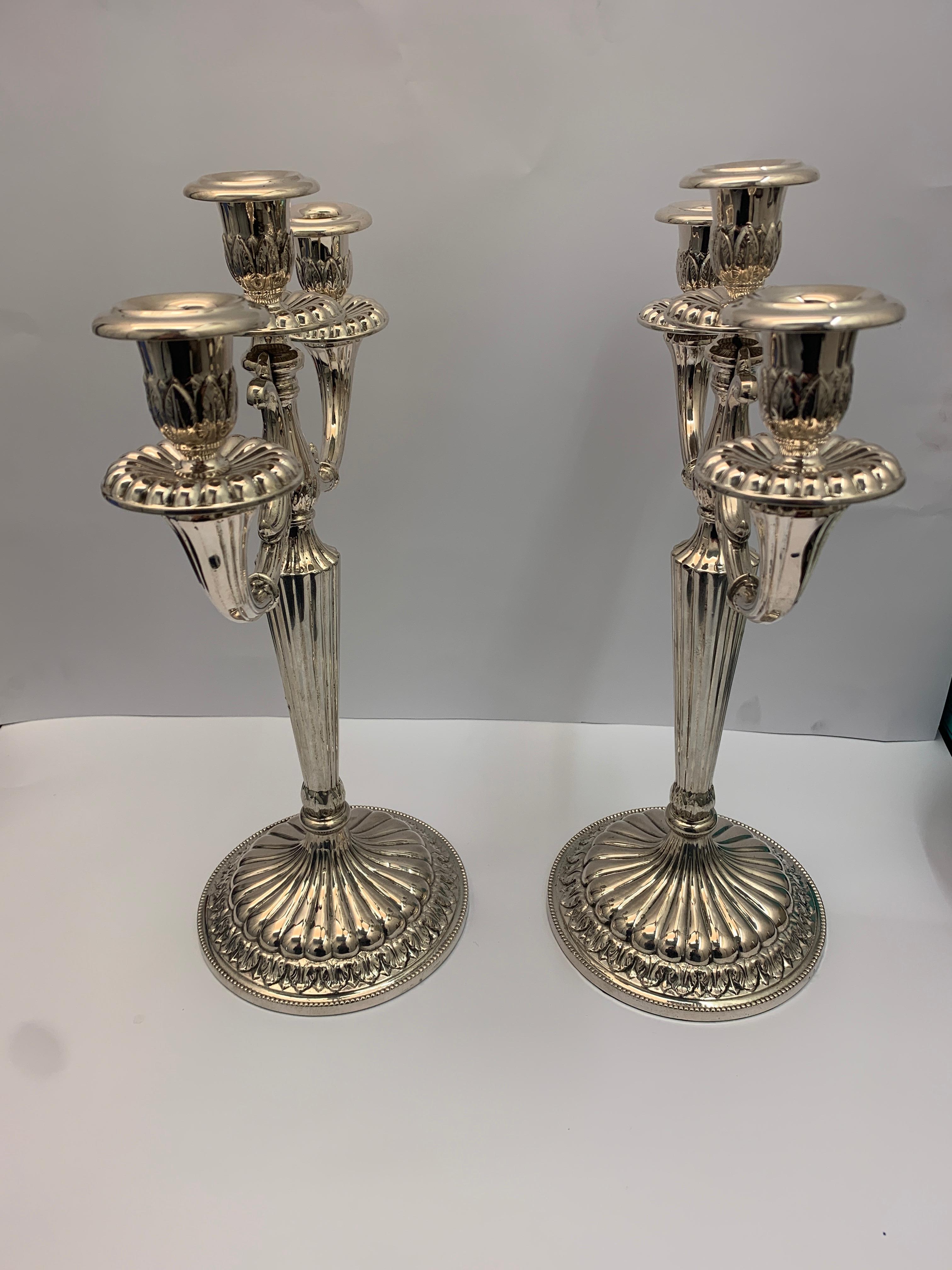 A pair of solid silver candelabra, made in Italy in 1950. Each candelabra has 3 candleholders with circular wax catchers, decorated with leaves and scrolls.