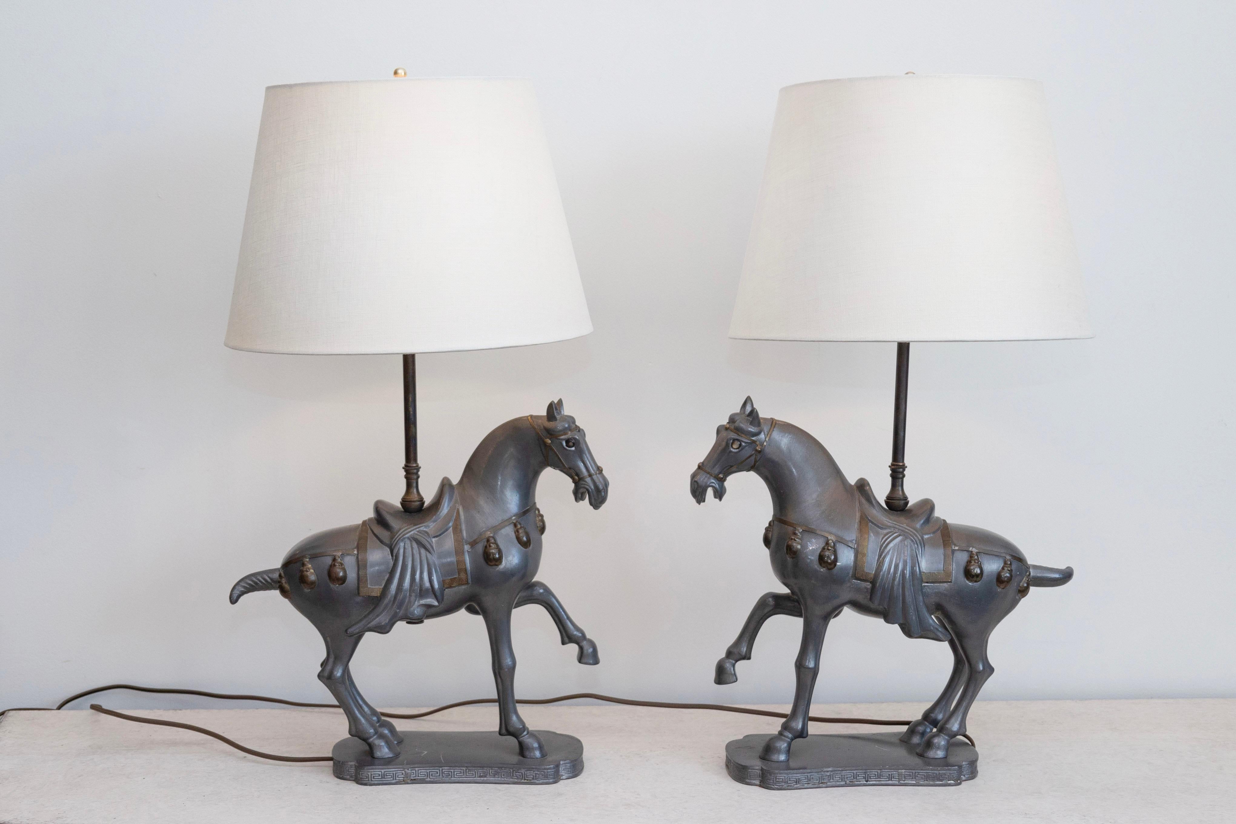 Cette paire de lampes de table saisissante présente des chevaux élégamment sculptés, inspirés des statues équestres de l'époque de la dynastie Tang, connues pour leur posture royale et leurs détails complexes. Les chevaux, en métal patiné foncé ou