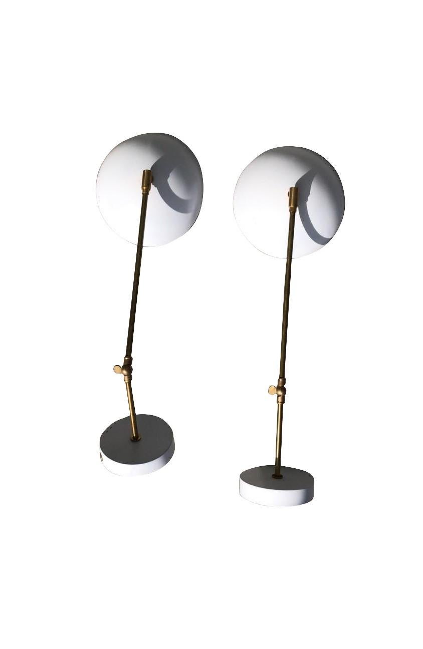 A vintage Mid-Century Modern Italian pair of wall appliques, sconces made of hand crafted brass with an adjustable arm and white metal shade, each lamp is featuring a one light socket. Produced by Stilnovo in good condition. The wires have been