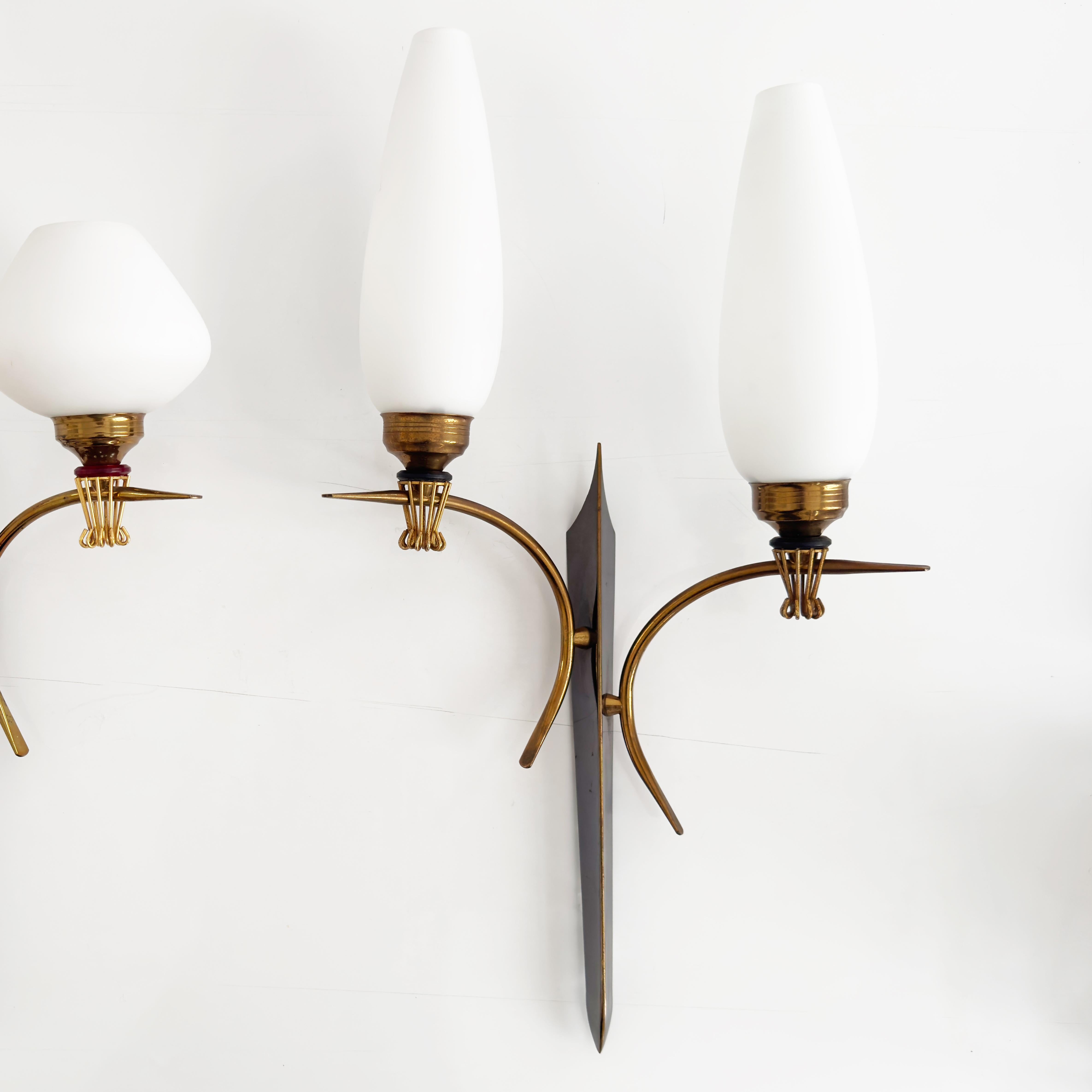 A beautiful example of mid-century lighting design, this sculptural pair of wall lamps from the 1960s feature a sleek brass structure with two gracefully arched arms. Each arm supports a satin-finish opaline glass shade, softly diffusing the light