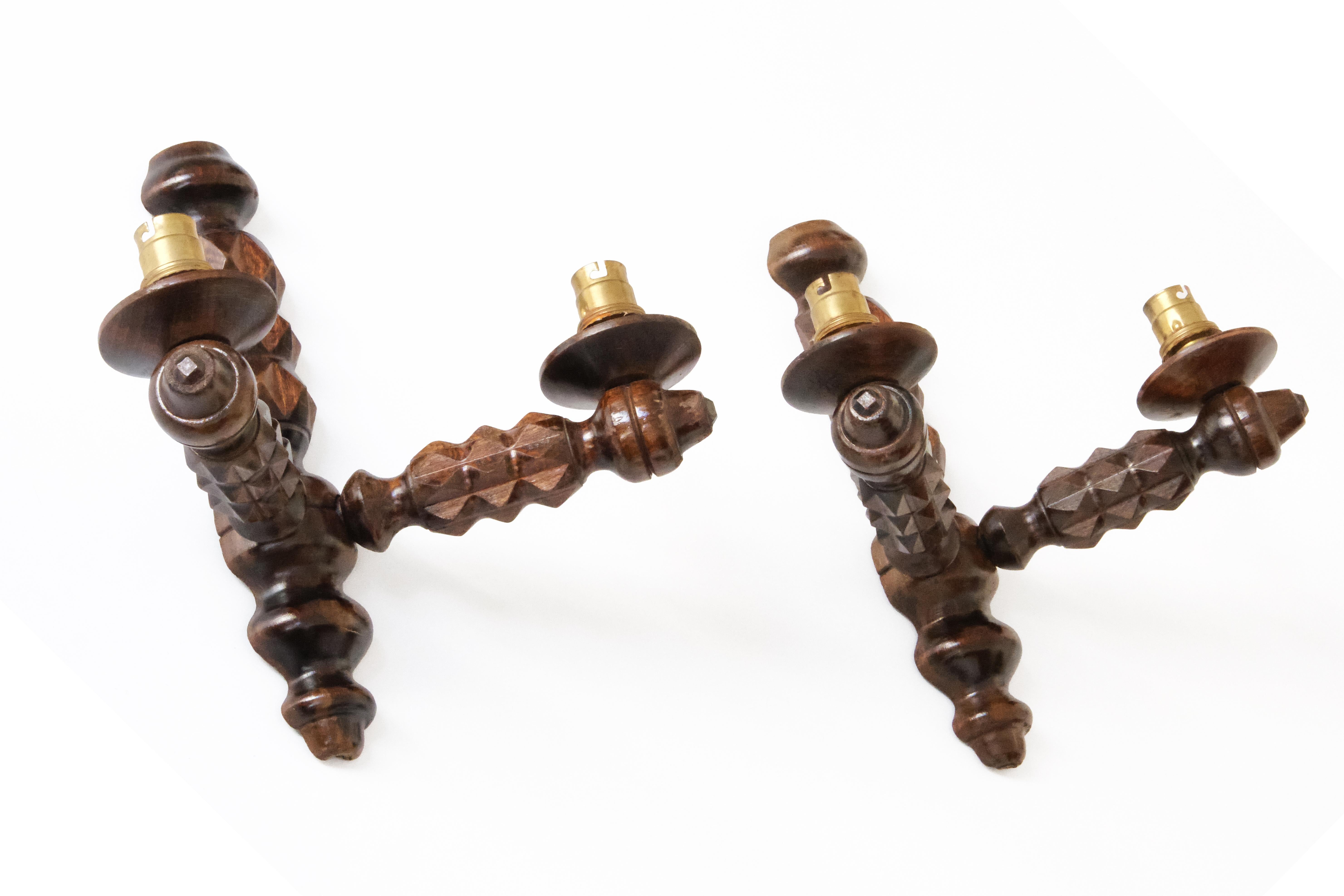 Un'impressionante coppia di applique scultoree, meticolosamente intagliate a mano probabilmente in legno di quercia. Ogni applique presenta un design geometrico e sfaccettato del gambo nello stile di Dudouyt, che ricorda l'artigianato tradizionale