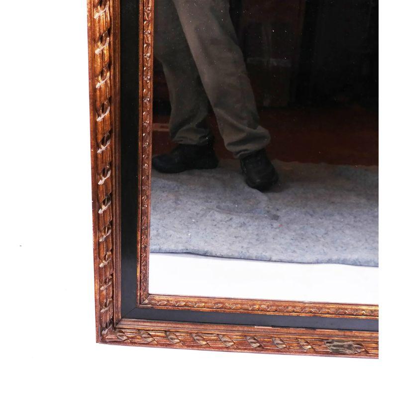 A parcel giltwood and ebonized mirror, dated 20th century. The rectangular mirror is framed with carved giltwood molding and alternates with an ebonized center between the two distinct carving designs.  A bit of natural wear adds to the beautiful