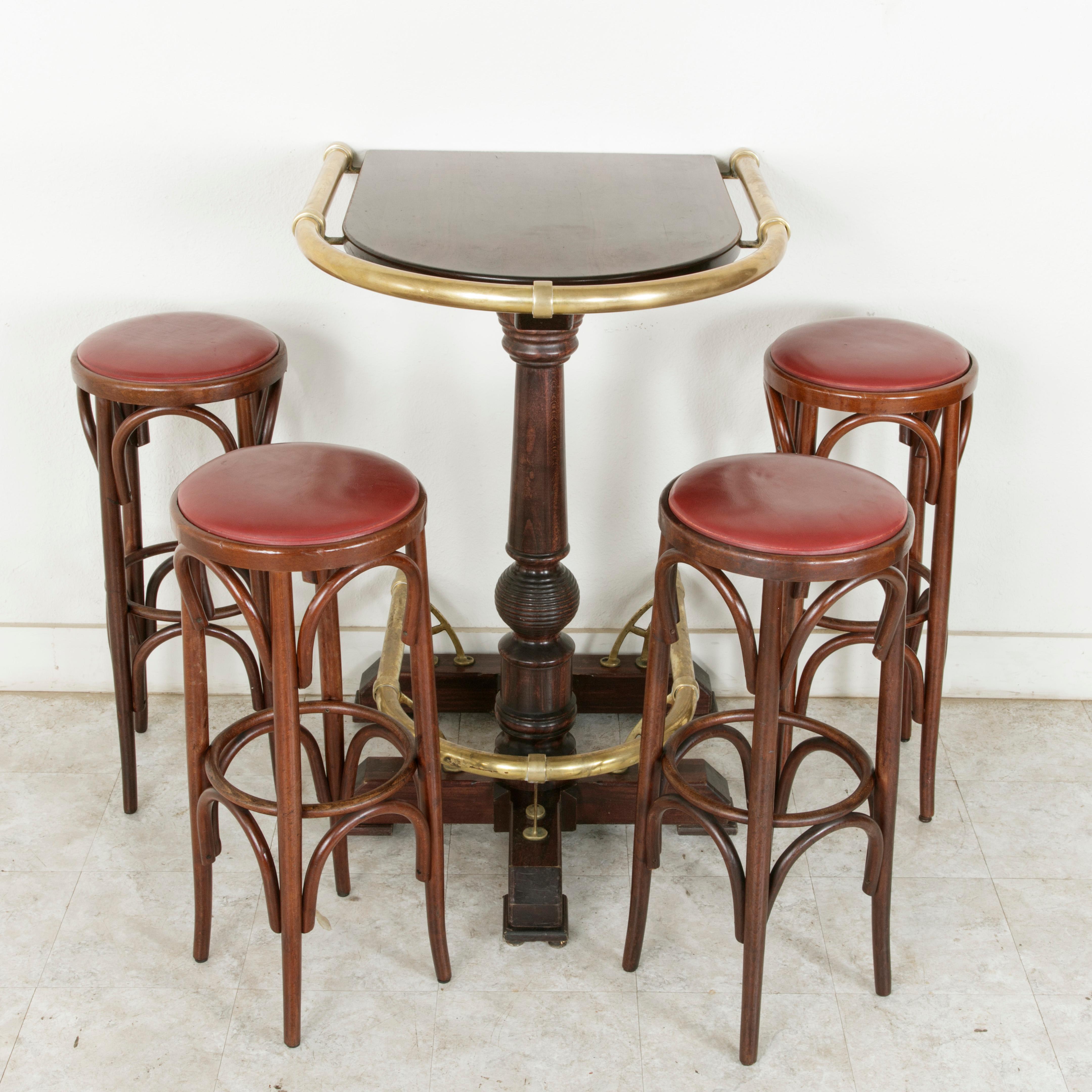 This 20th century French brasserie booth, complete with a high top table and four bar stools, once served in a Parisian brasserie. The table originally stood against a wall and features a central turned pillar on a stretcher base and large brass
