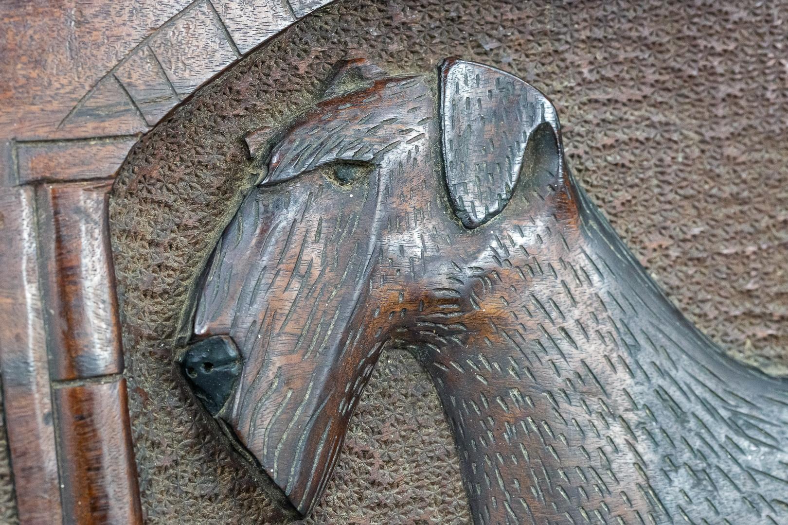 Wunderschöne reliefgeschnitzte Airedale-Terrier-Plakette aus dem 20. Jahrhundert, links die Siegerrosette und rechts die Siegertrophäe. Der Siegerhund steht stolz in der Mitte, aufwendige Details im gesamten Bild. England 20. Jahrhundert, auf der