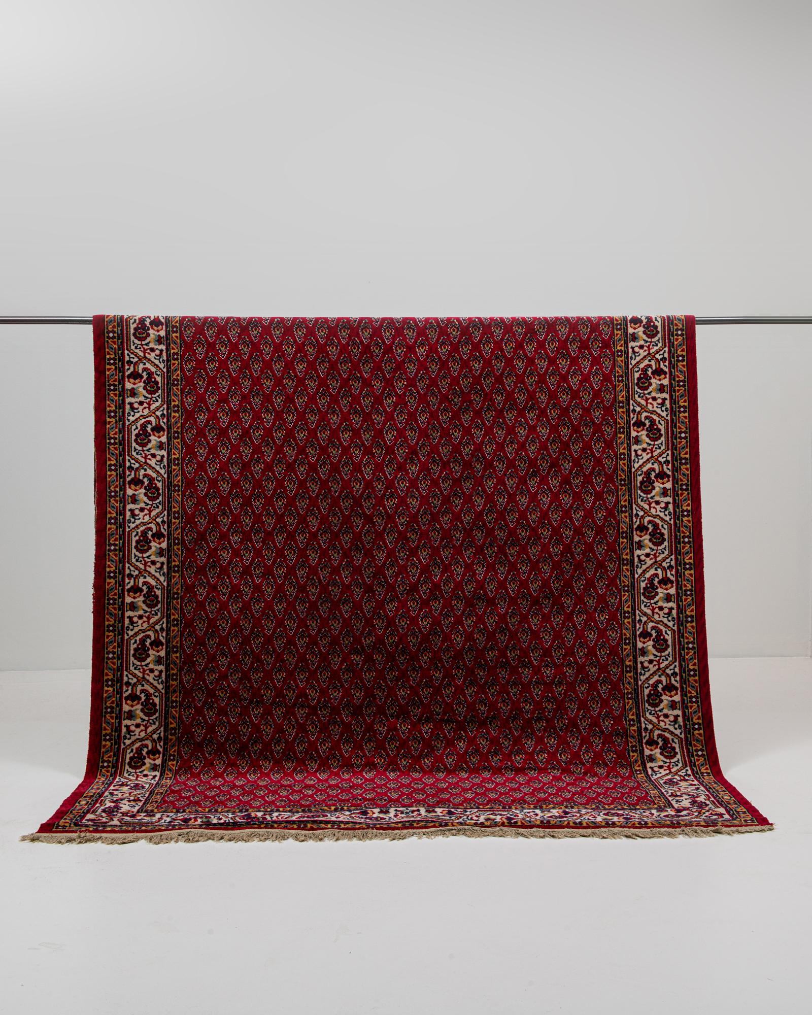 Dieser persische Orientteppich aus dem 20. Jahrhundert zeigt ein leuchtend rotes Feld mit einem sich wiederholenden Boteh-Motiv, das ein rhythmisches, juwelenartiges Muster auf seiner Oberfläche bildet. Die detaillierte Bordüre zeigt traditionelle