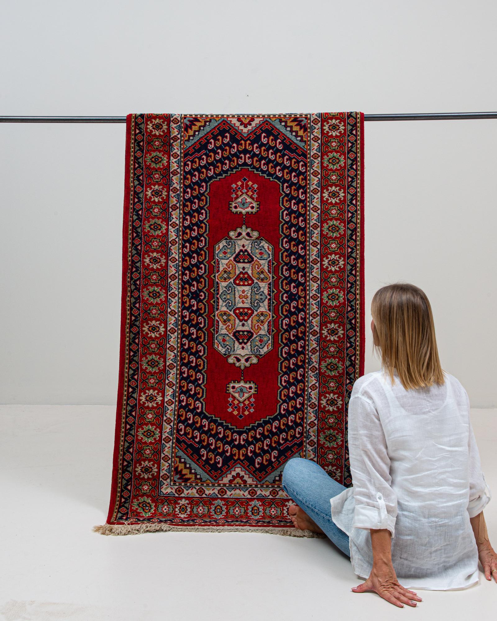 Dieser persische Orientteppich aus dem 20. Jahrhundert zeichnet sich durch ein auffälliges Medaillonmuster auf einem leuchtend roten Feld aus, das mit komplizierten geometrischen und floralen Motiven angereichert ist und die traditionelle persische