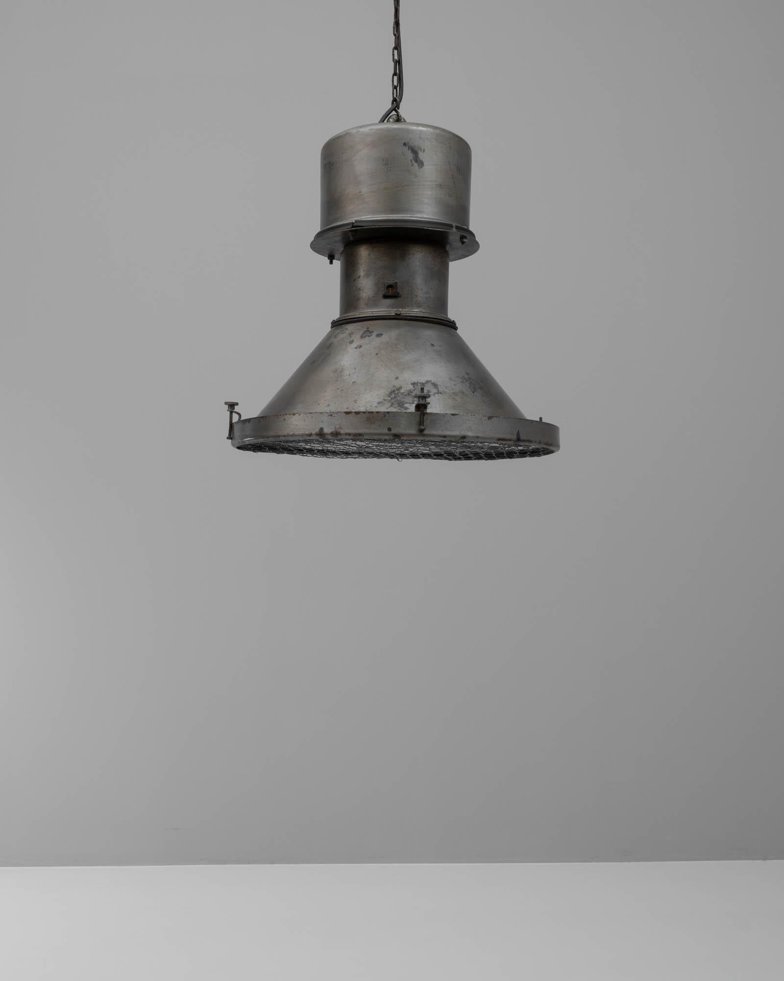 Cette lampe suspendue en métal polonais du 20e siècle dégage un charme industriel à la fois brut et raffiné. Le corps de la lampe est une construction métallique robuste, dont la surface présente l'usure honnête et la patine distinctive de son passé