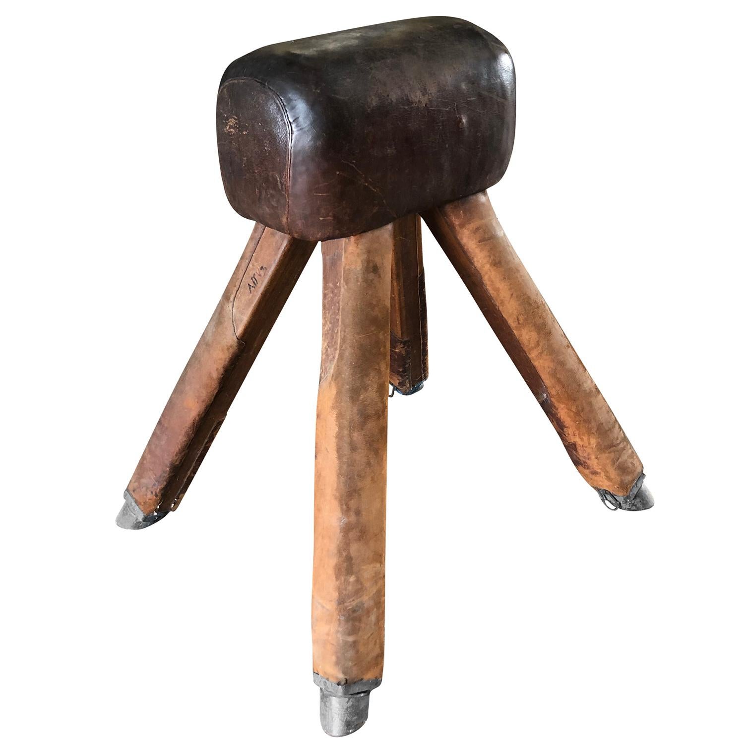A dark-brown, vintage French artistic gymnastics apparatus or pommel horse with solid wooden legs and a leather covered sitting saddle, in good condition with patina. The legs of the pommel horse are supported by four metal feet. Wear consistent