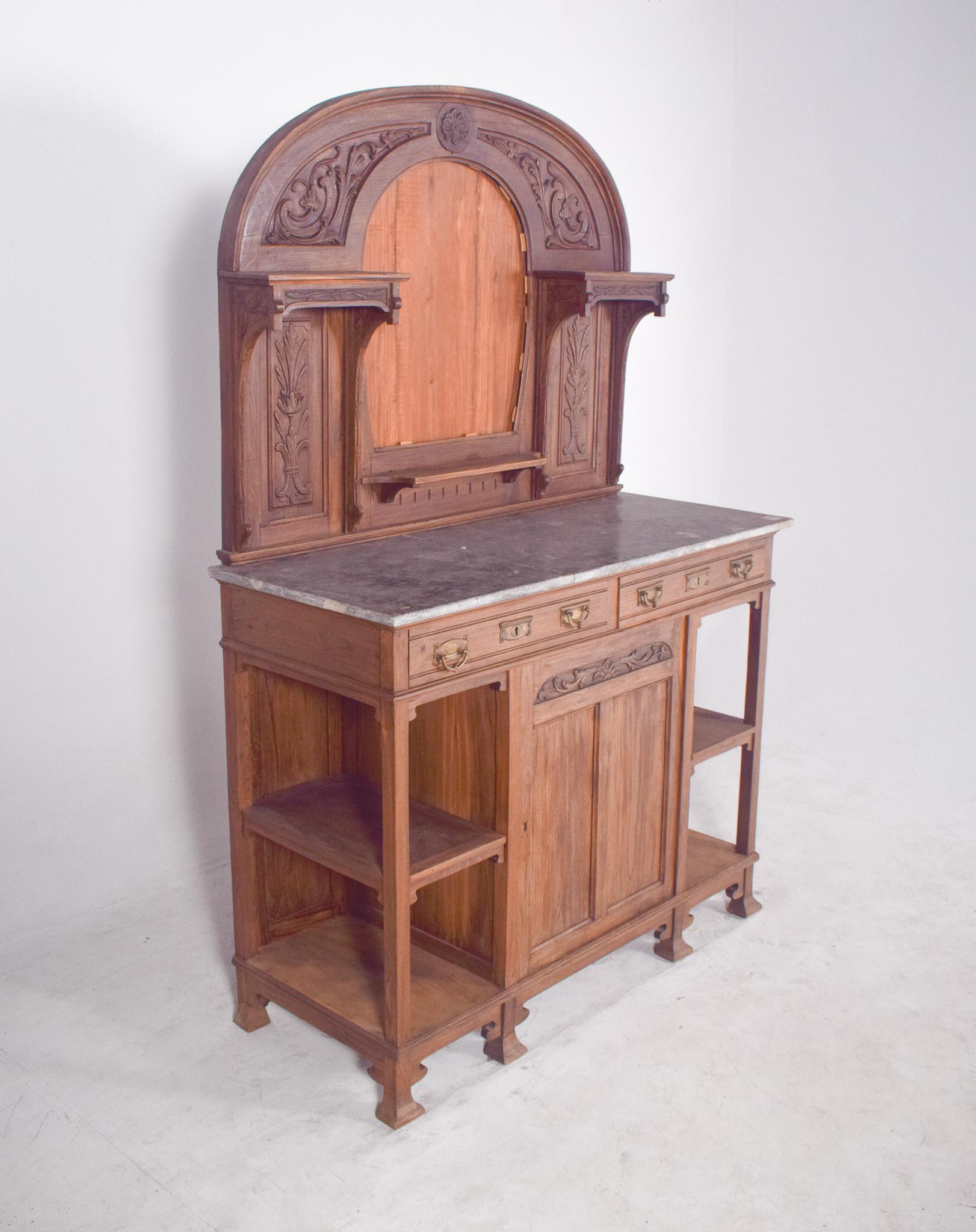 High Art Nouveau sideboard. The top features a central arch with floral elements carved in relief, as well as decorative shelves on the sides to support small objects or crockery.
It has a light marble top, three drawers with bronze metal handles