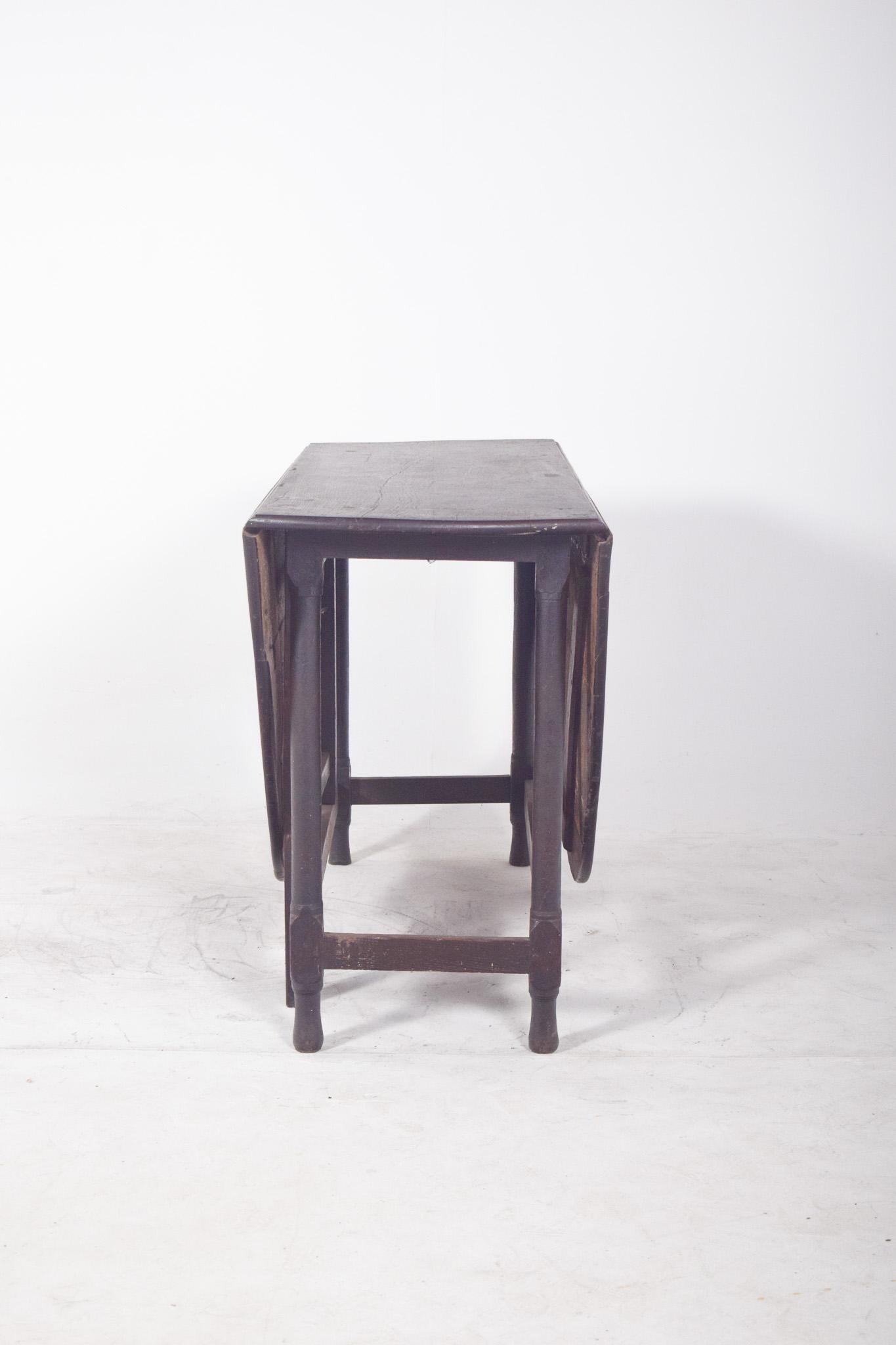 Oval-top table. In dark wood, with an oval top divided into three sections, a fixed centre section and two movable side sections that fold down gracefully when not in use. The structure rests on turned legs with cross reinforcement, providing