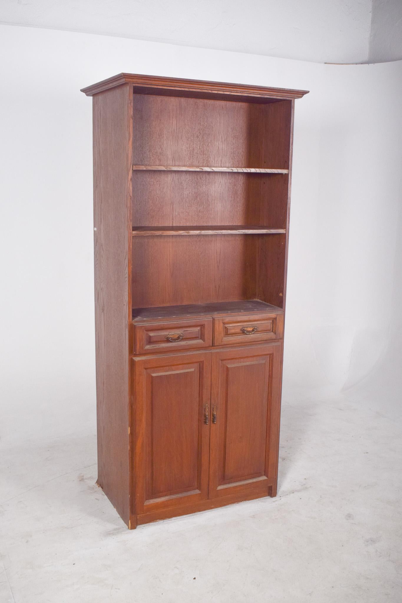 Mobile libreria con ripiani, ante e cassetti. Il piano è dotato di tre ripiani fissi, ideali per esporre libri, oggetti decorativi o utensili di uso quotidiano. La base del mobile è composta da due cassetti con maniglie decorative in metallo,