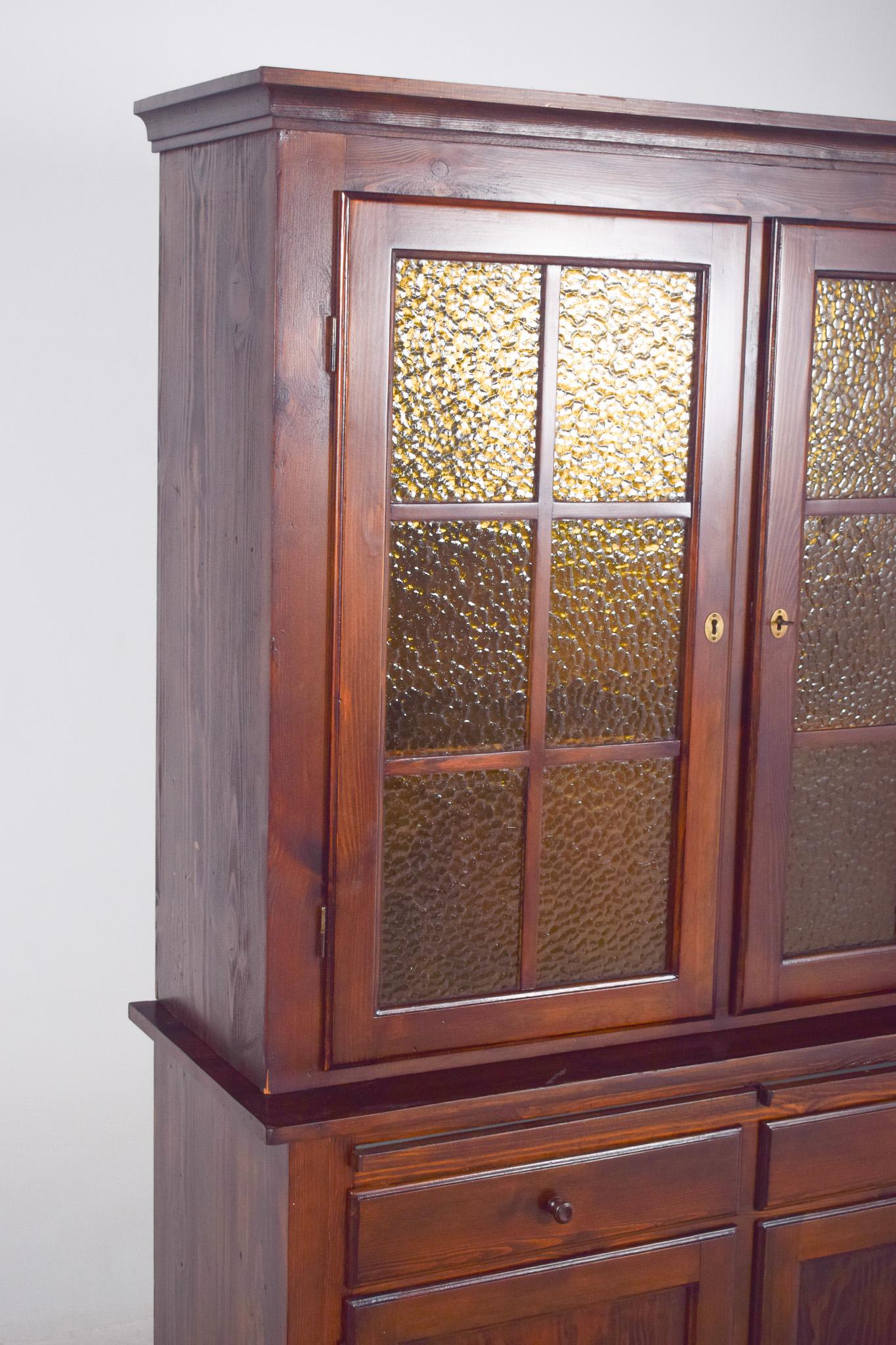 Two-body display cabinet. An imposing and functional piece characterised by the beauty of solid wood and the harmony between rusticity and elegance. The top is made up of two glazed doors with wooden mouldings and cross partitions. The textured