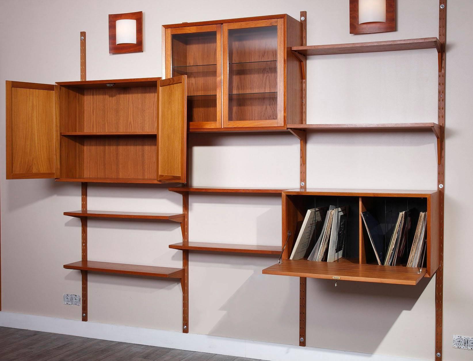 Modular wall system designed by Poul Cadovius in the 1950s, crafted in teak, provided with wooden fixations. It is composed of four vertical ladders with six shelves and three containers as follow: One container with lateral doors, one container